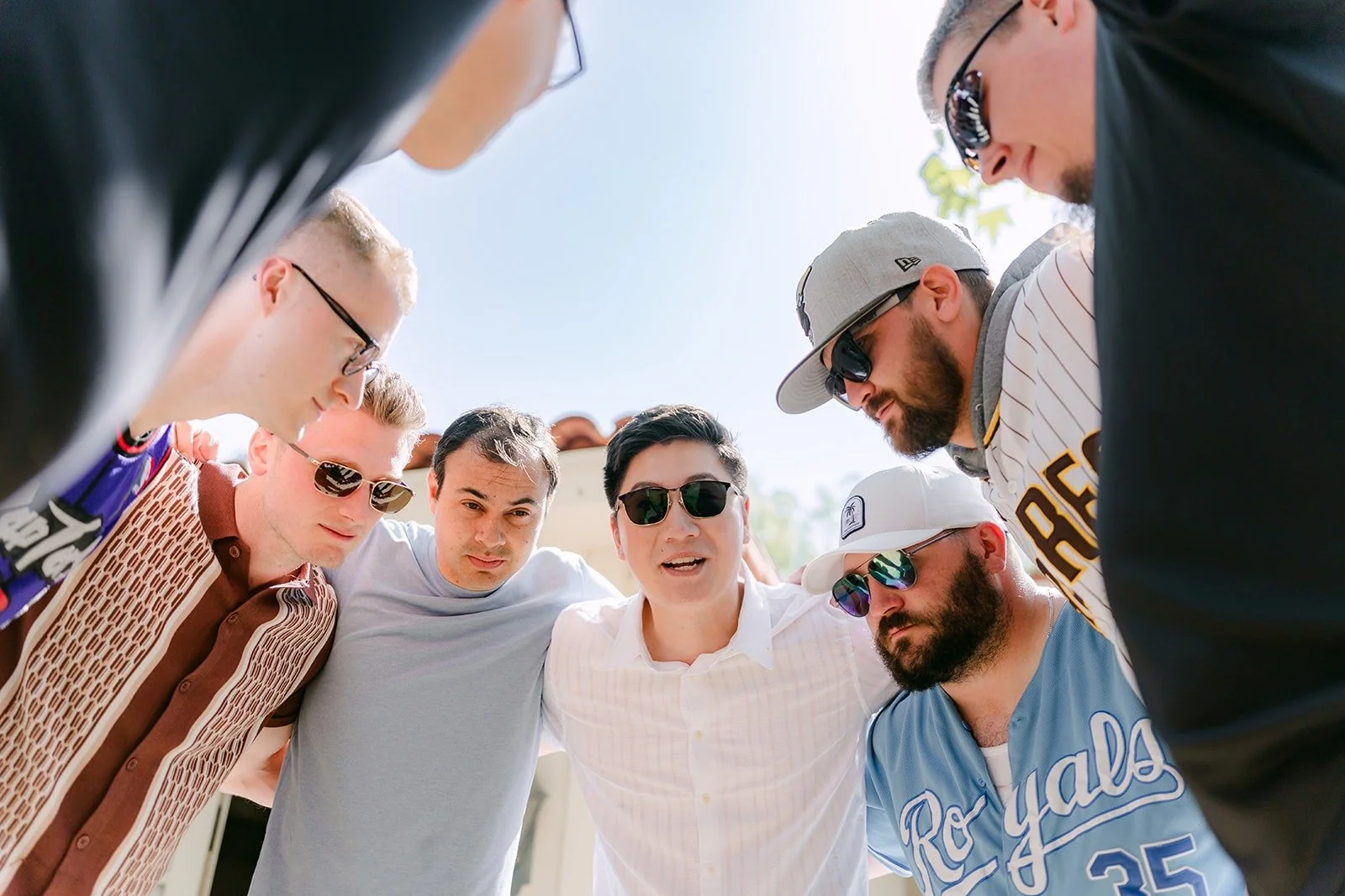 Zach and his groomsmen leaning into a huddle in game day shirts and caps at Rancho Bernardo Inn