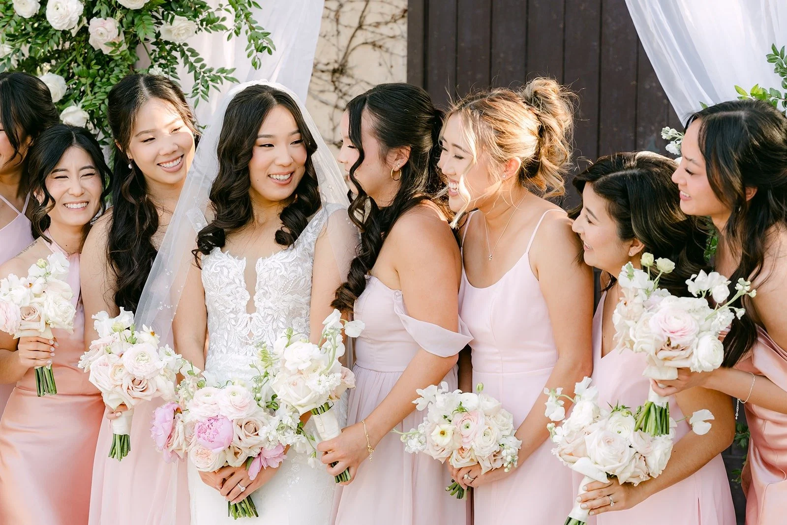 Kelli laughing with her bridesmaids as they hold their bouquets close, photographed by One and Only Production