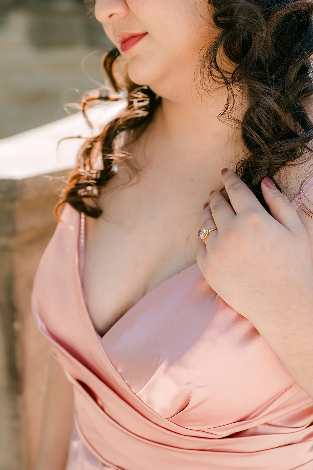 Detail of Saira's hand resting at the neckline of her blush satin dress.