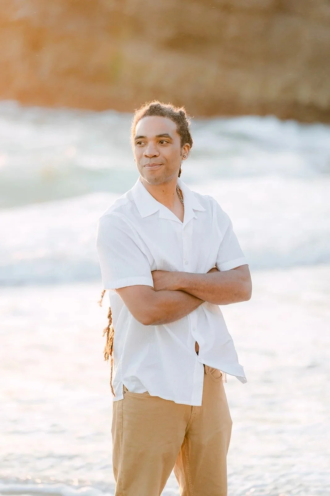 Michael in a white shirt with his arms crossed on the beach.