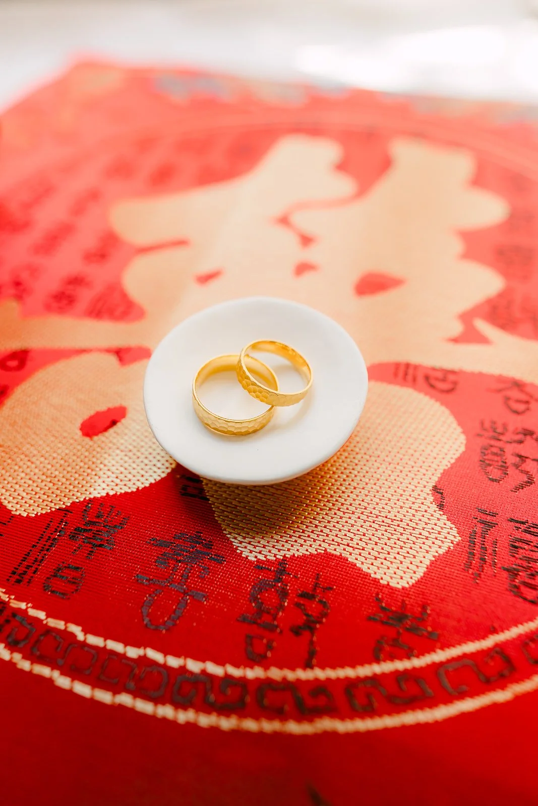 Two gold rings resting in a small dish on a red double happiness cloth.