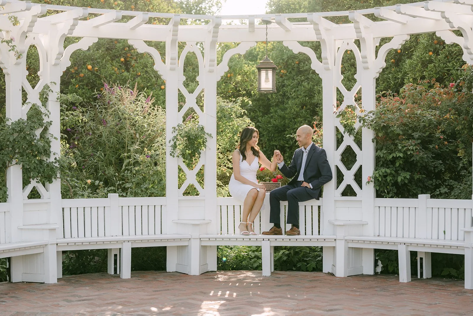 Francesca and Daniel sit together on the bench inside the white gazebo.