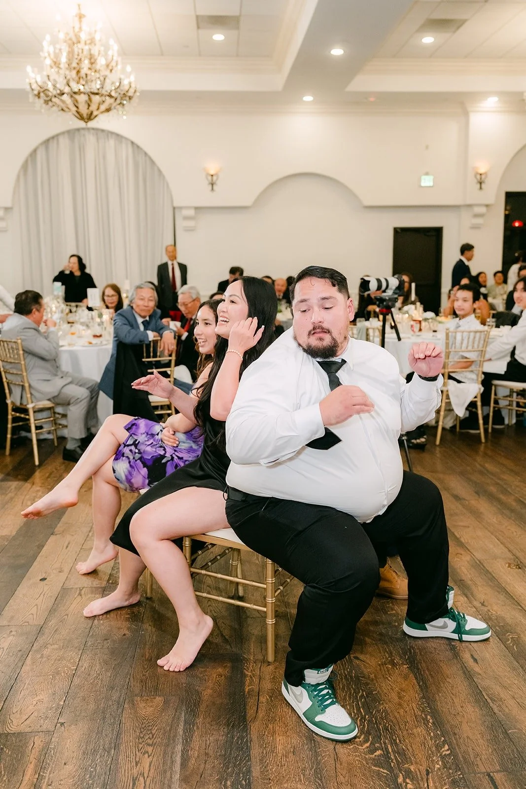 A groomsman seated in the middle of a game as guests laugh