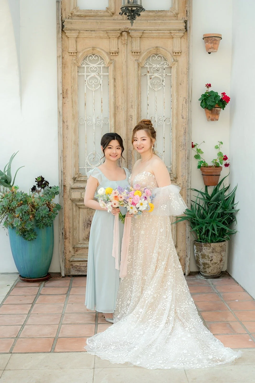 Joanna and a bridesmaid in dusty blue in front of the carved door, photographed by One and Only Production
