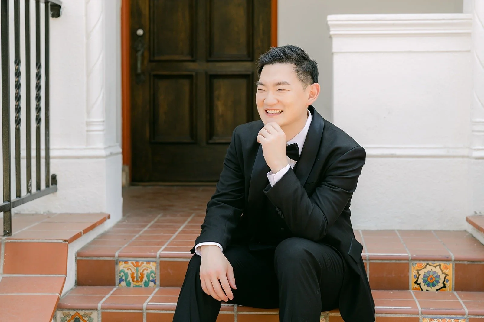 Sam seated on the mansion steps in his black tuxedo