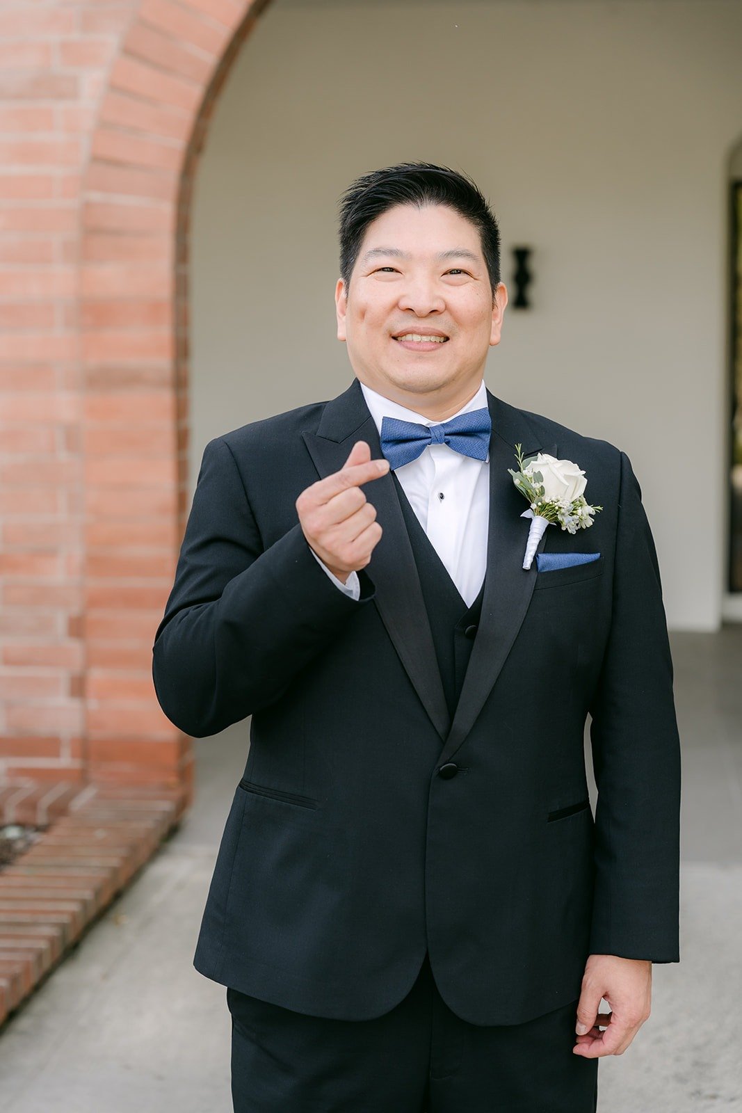 Jay in his tuxedo smiling beneath a brick arch, photographed by One and Only Production