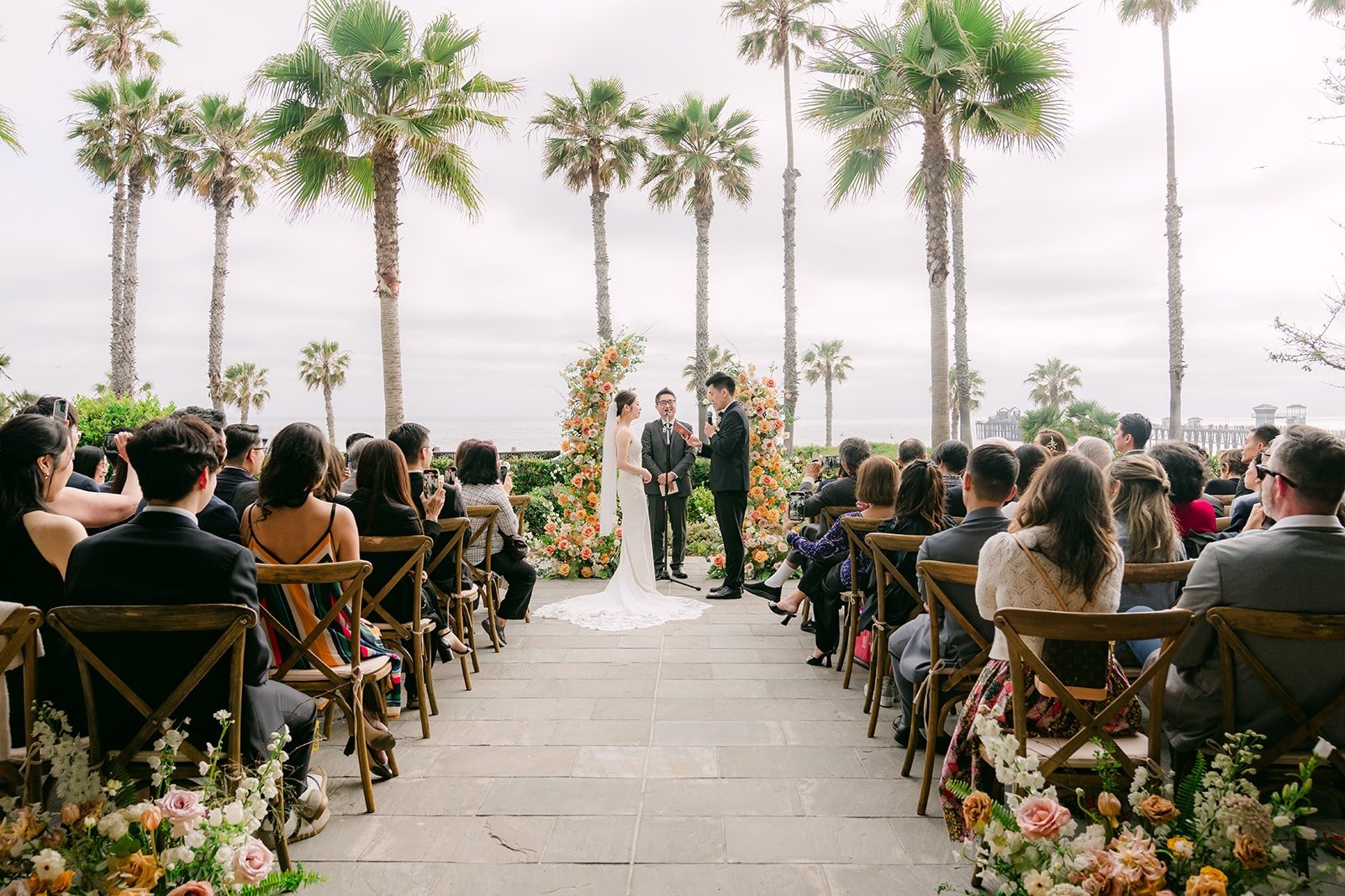 Wide view of the ceremony with guests seated along the aisle and palms overhead