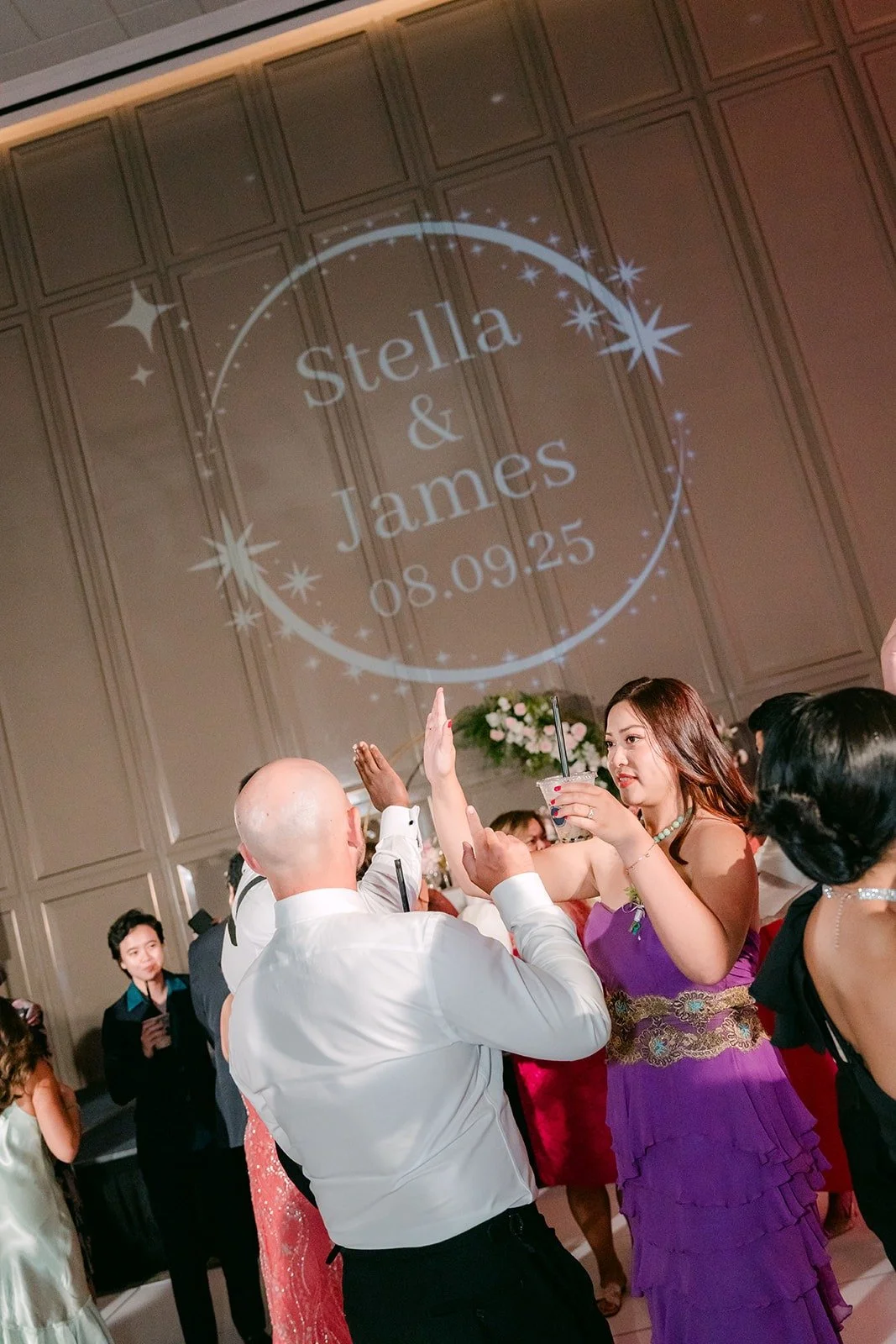 Guests dancing under a Stella and James monogram projected on the ballroom wall