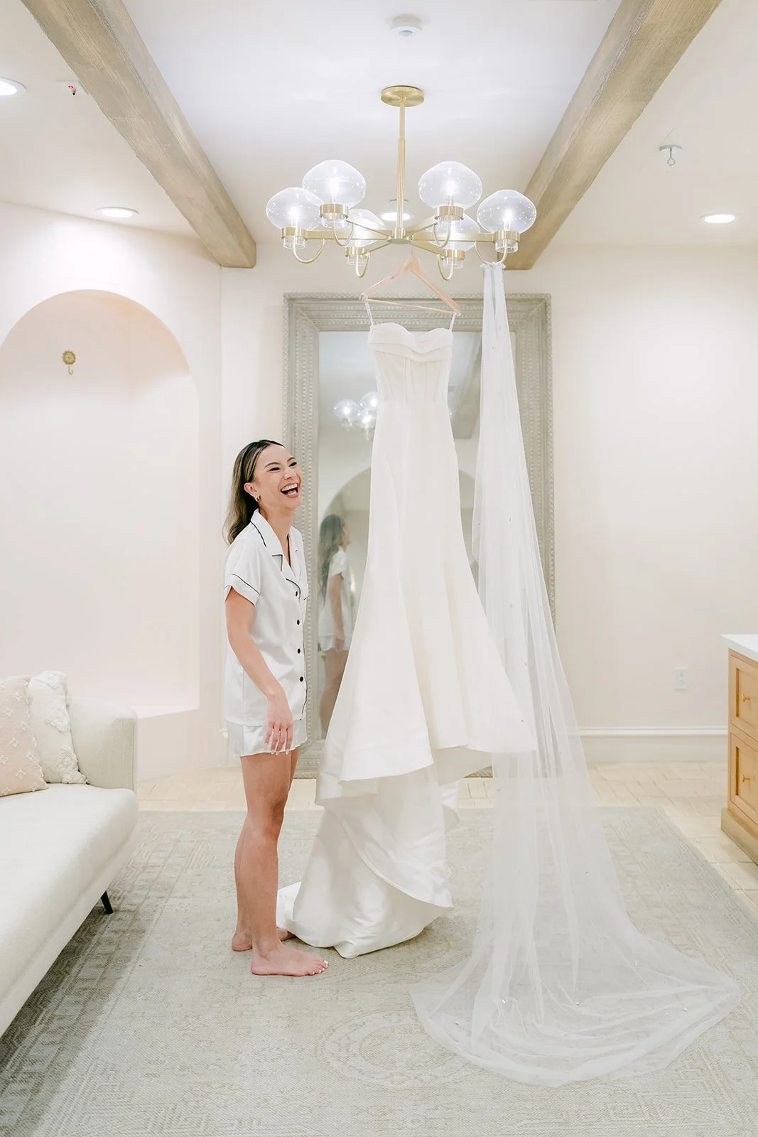 Kieu in white pajamas beside her gown hanging from the chandelier in the Serra Plaza bridal suite