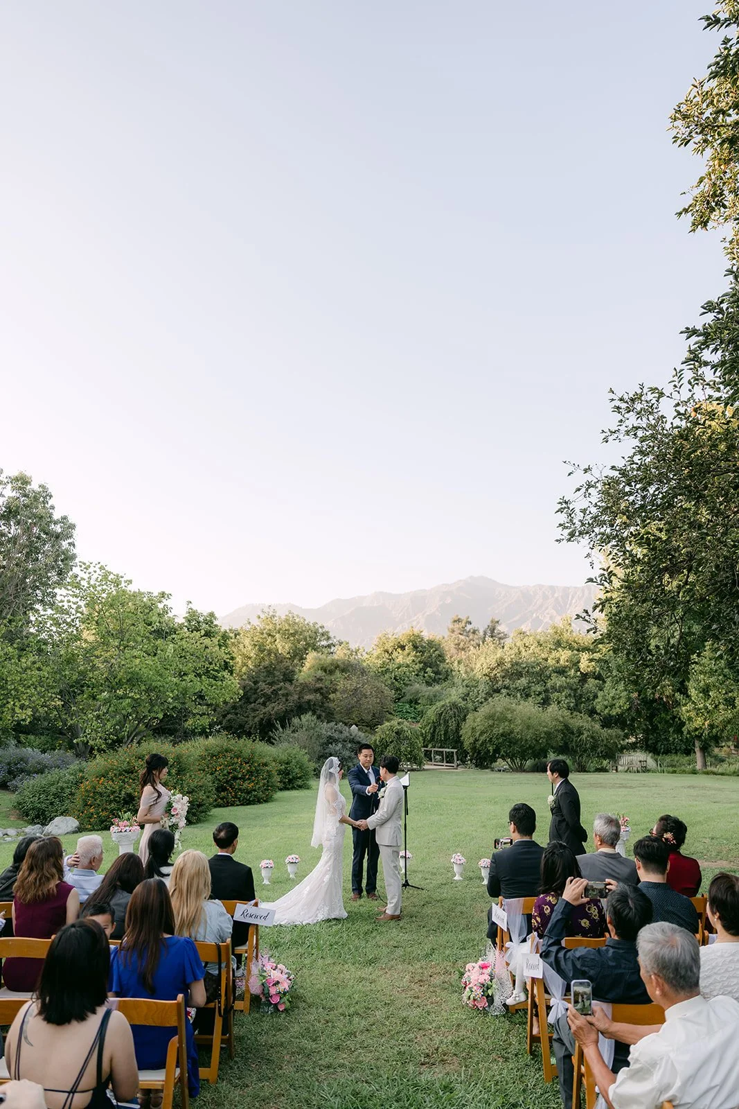 Wide view of the ceremony from behind the guests under the trees.