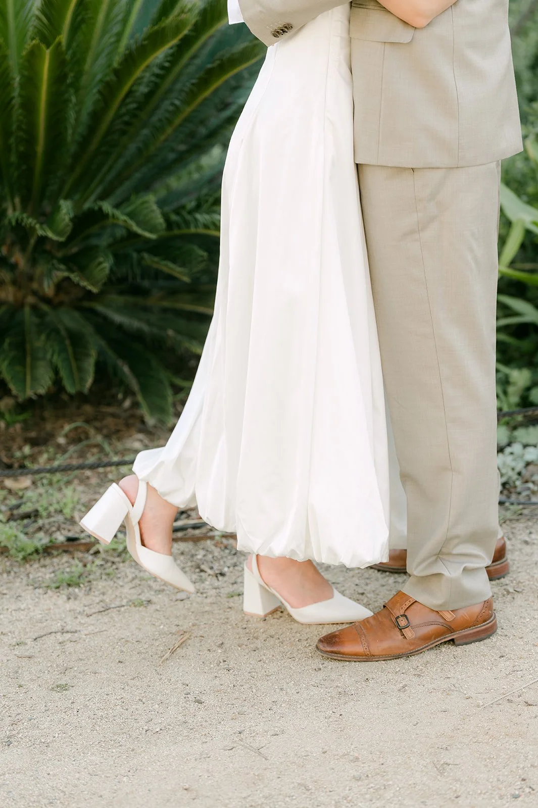 Detail of Kim's white heels and Vincent's brown shoes as they stand close on the path.
