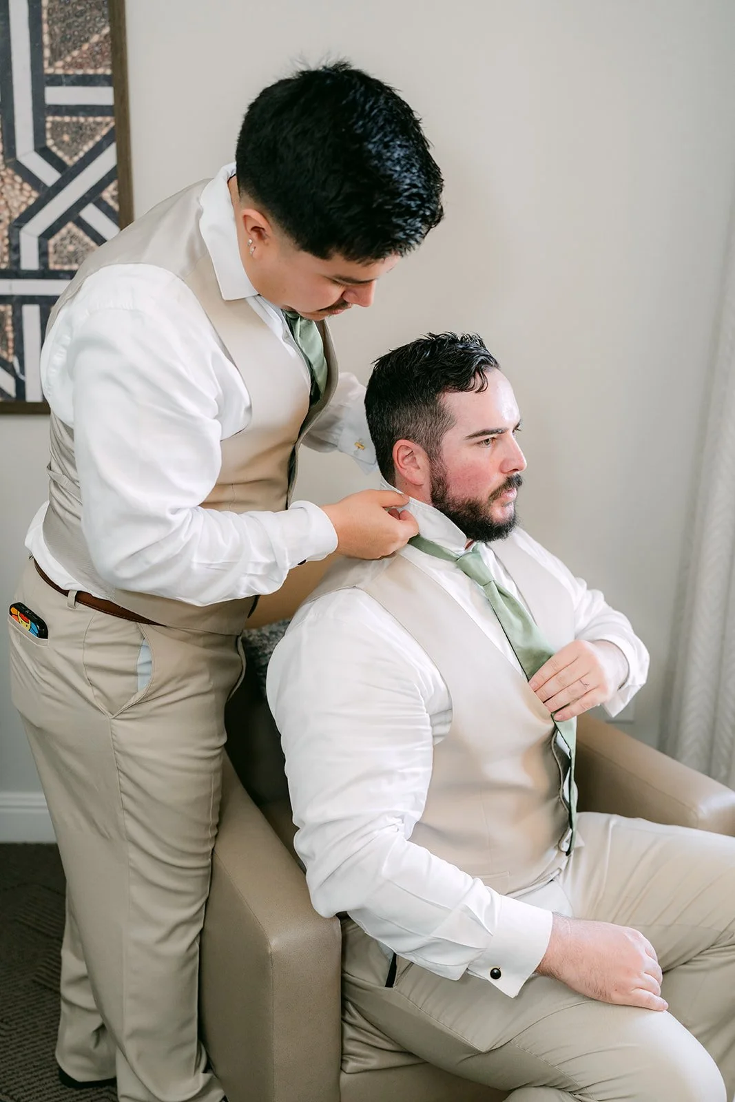 A groomsman helping Cody with his tan suit.