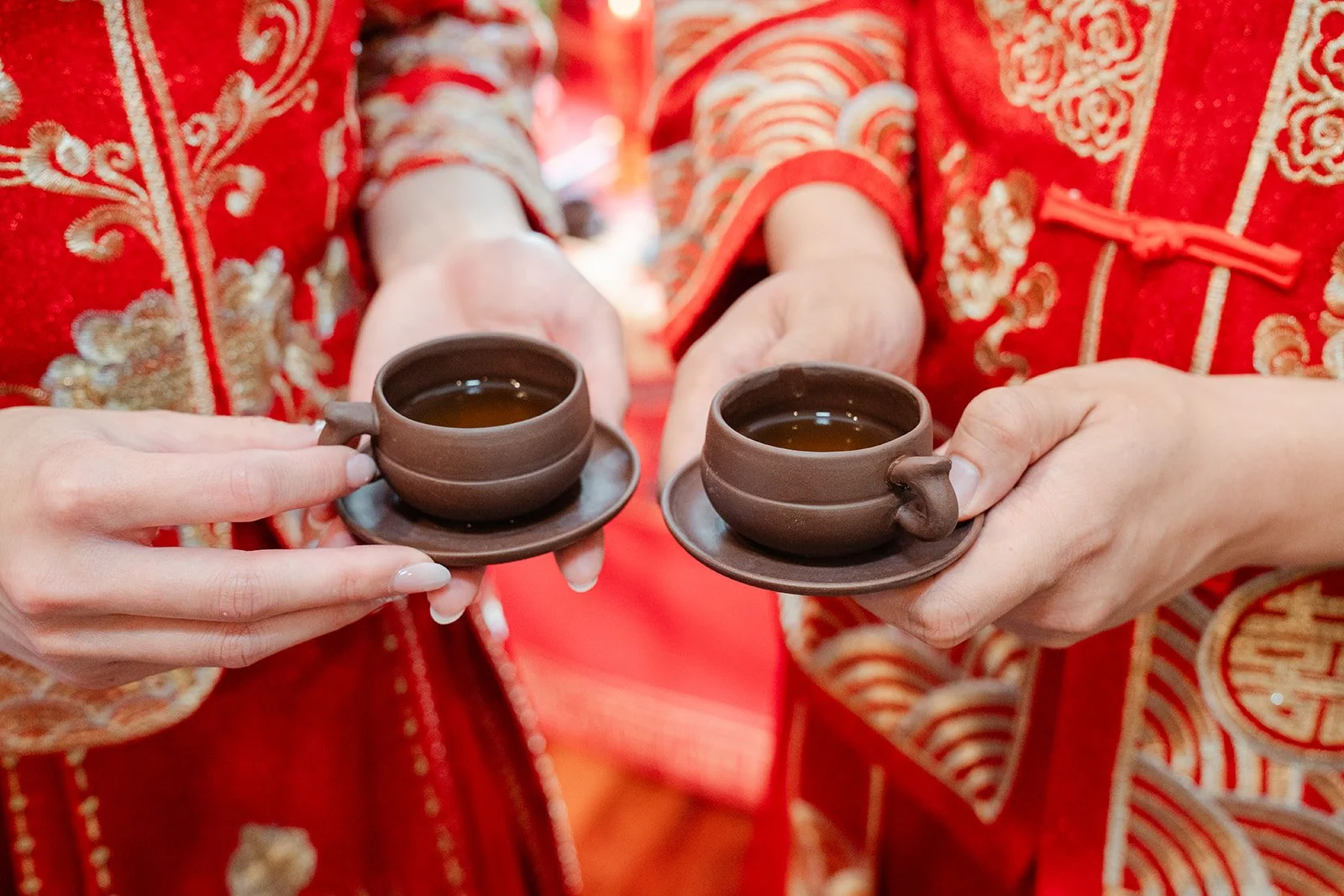 The couple's hands holding teacups during the tea ceremony.