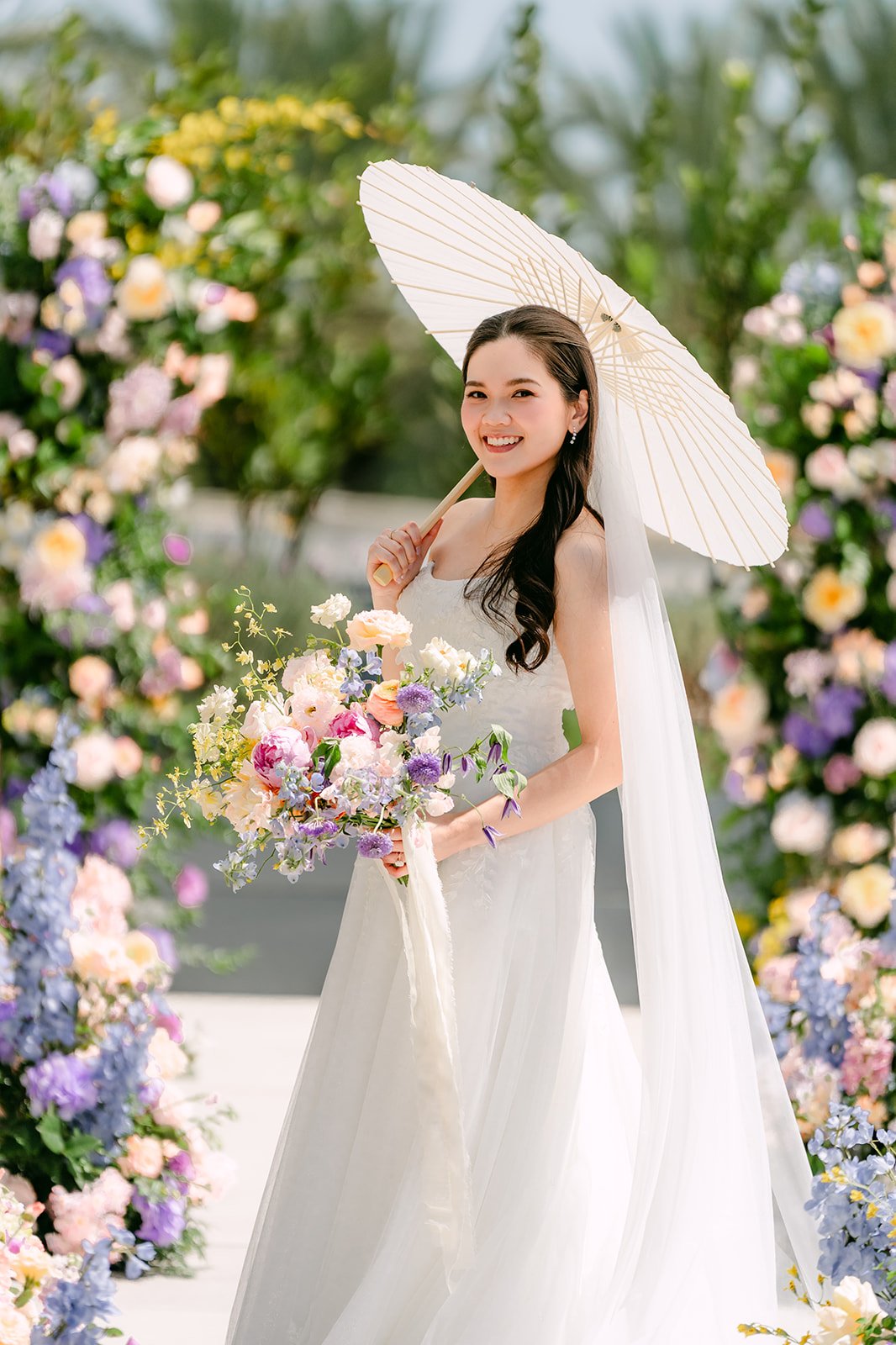 Bride with a white paper parasol among pastel flowers in the Serenity Garden