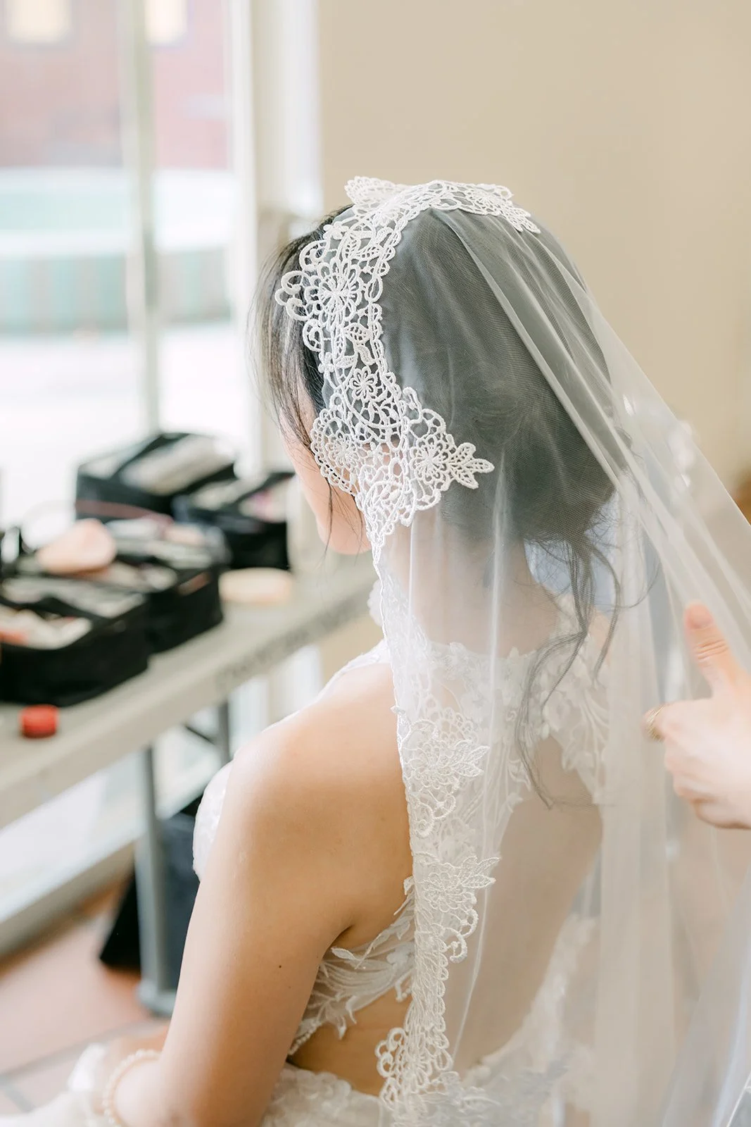 Elaine's veil being placed, seen from behind at the vanity.