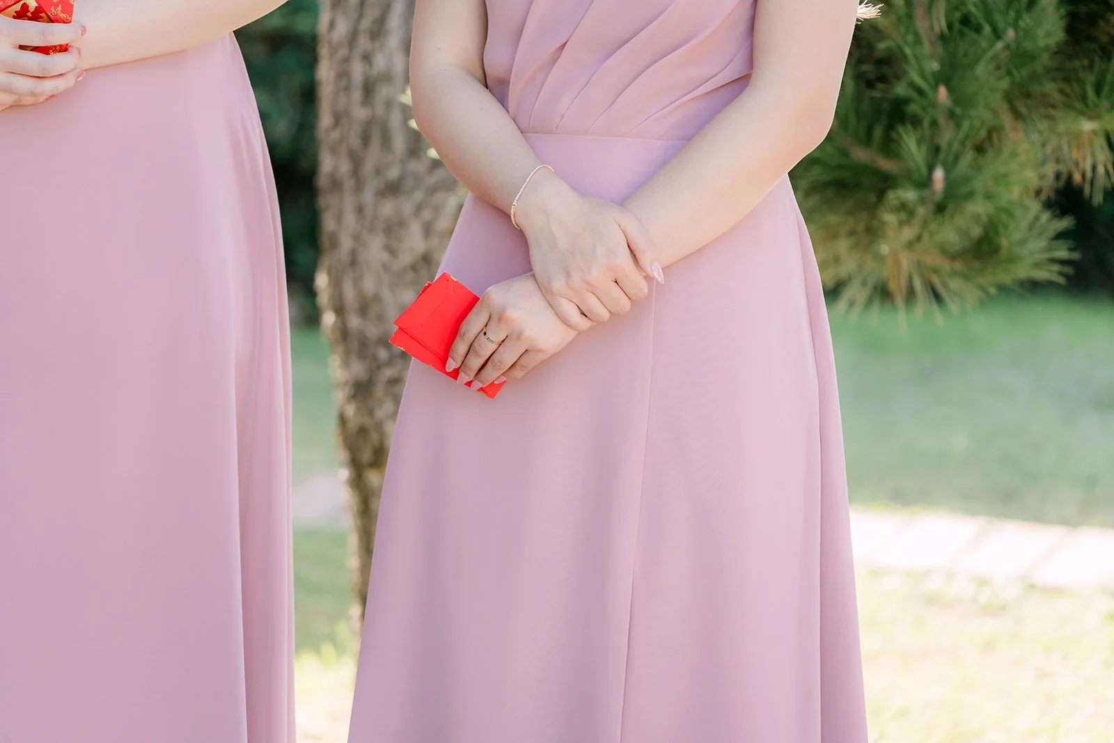 A bridesmaid in pink holding red envelopes.