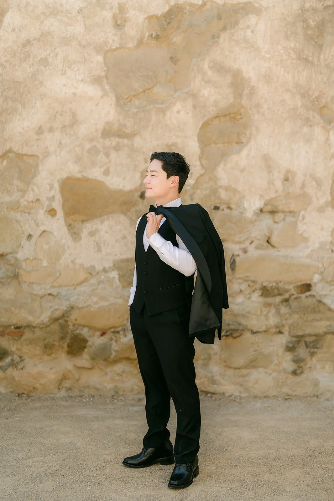 Min Soo in a black tuxedo against an old stone wall at Mission San Juan Capistrano
