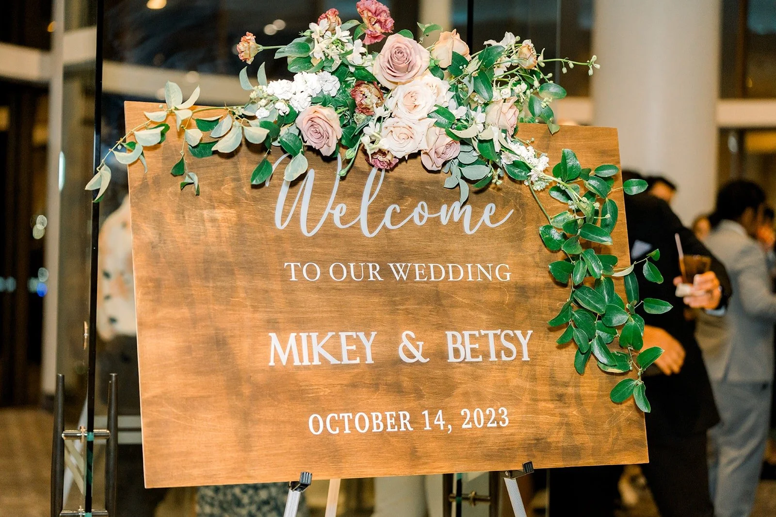 A wooden welcome sign for Mikey and Betsy with blush and white flowers