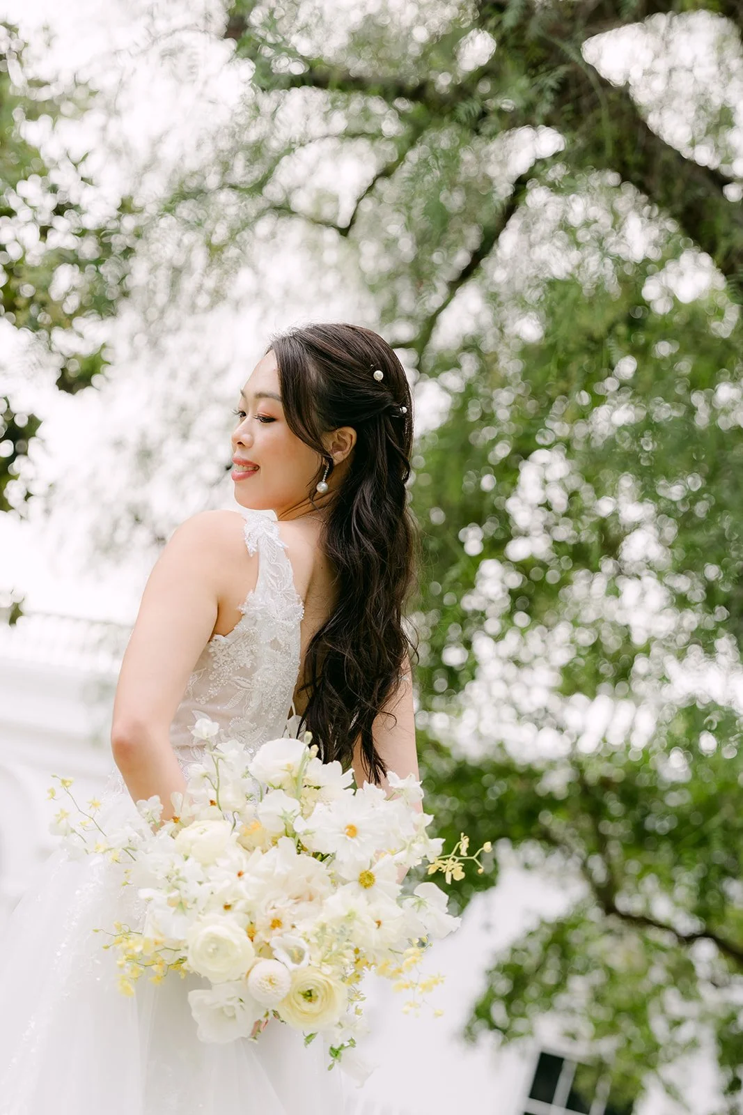 Jenny holding her bouquet and looking down under the trees, photographed by One and Only Production.