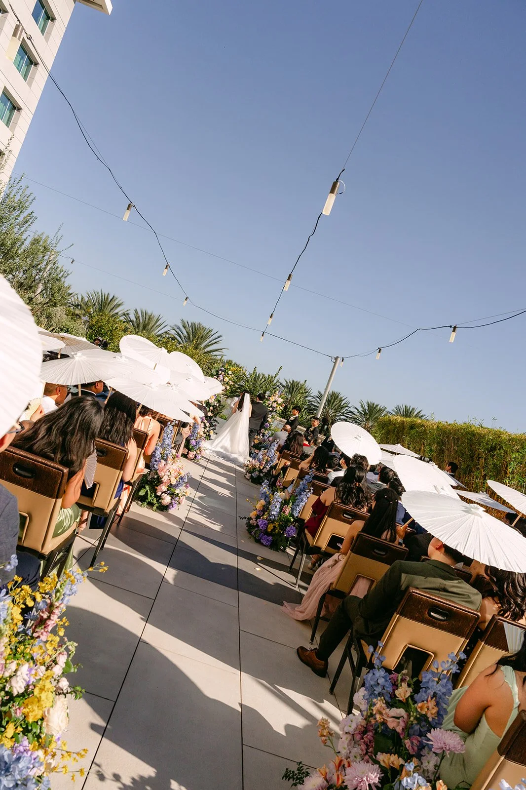Guests with white parasols seated for the outdoor ceremony