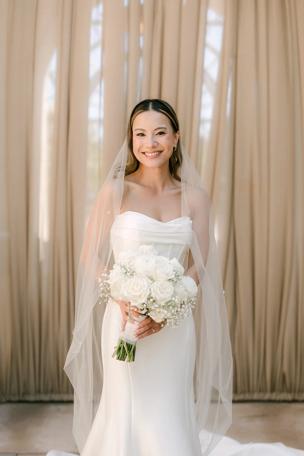 Portrait of the bride smiling in her veil holding a white bouquet
