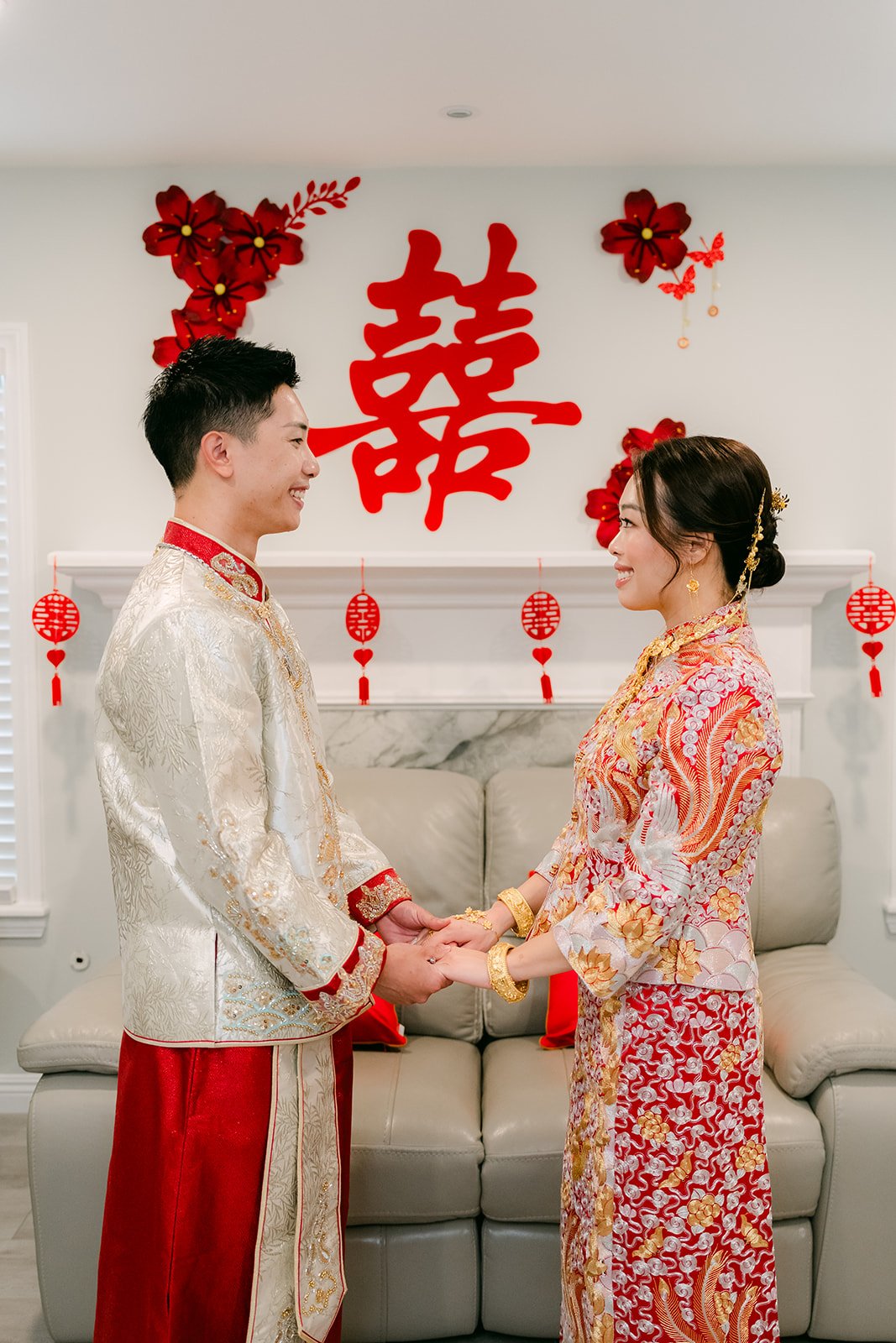 A bride and groom holding hands in front of a double happiness backdrop.