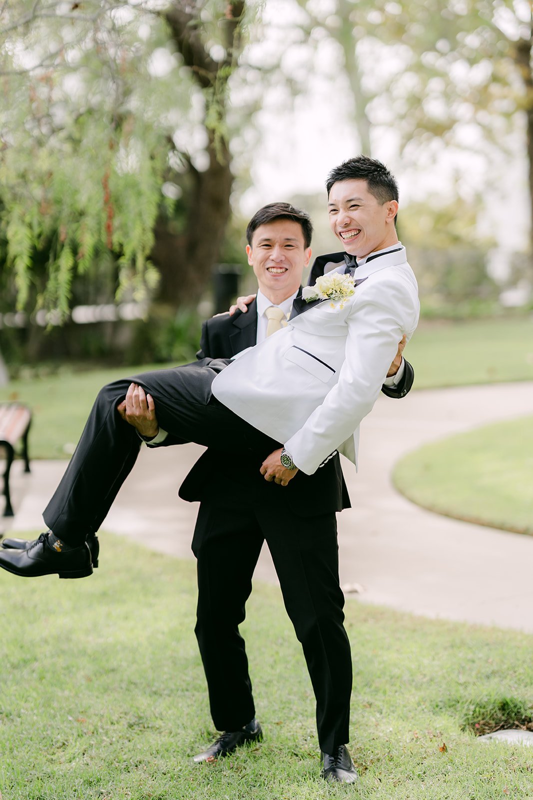 A groomsman lifting Ryan off his feet on the lawn.