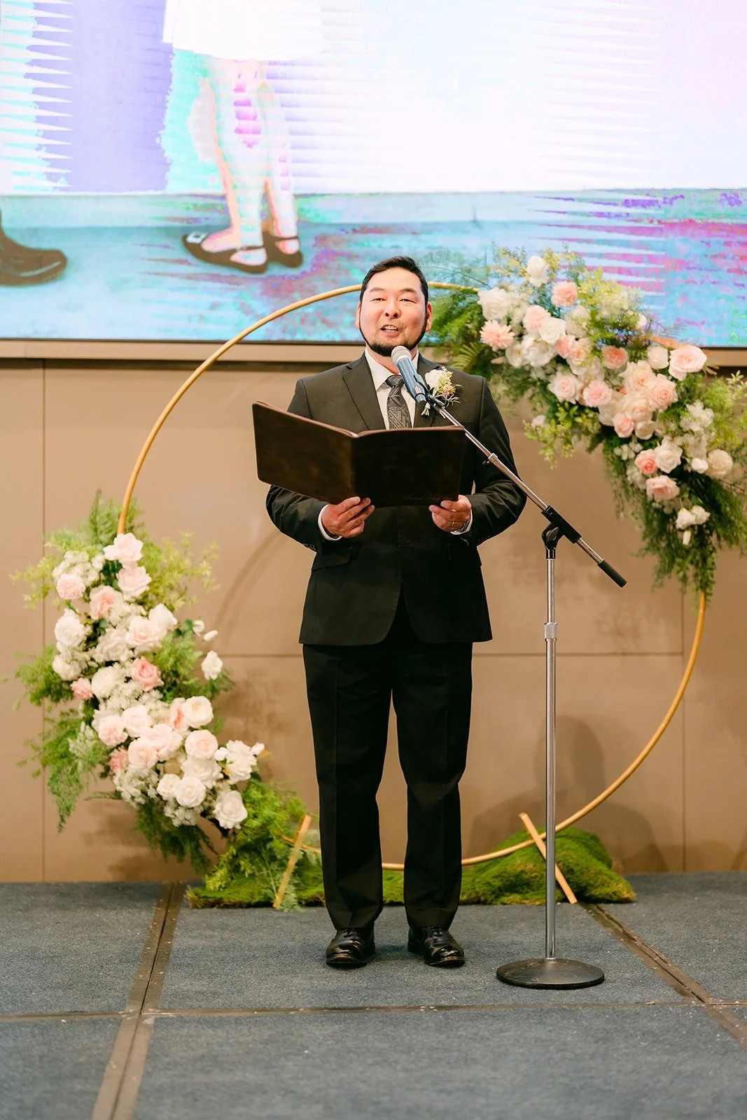 The officiant standing at the arch with a book at the front of the ballroom