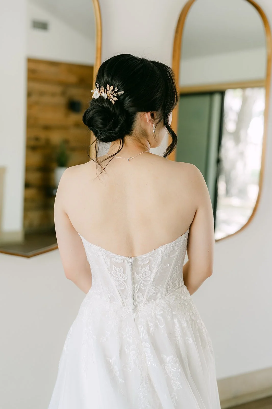 Bride's low updo and strapless gown framed by arched mirrors
