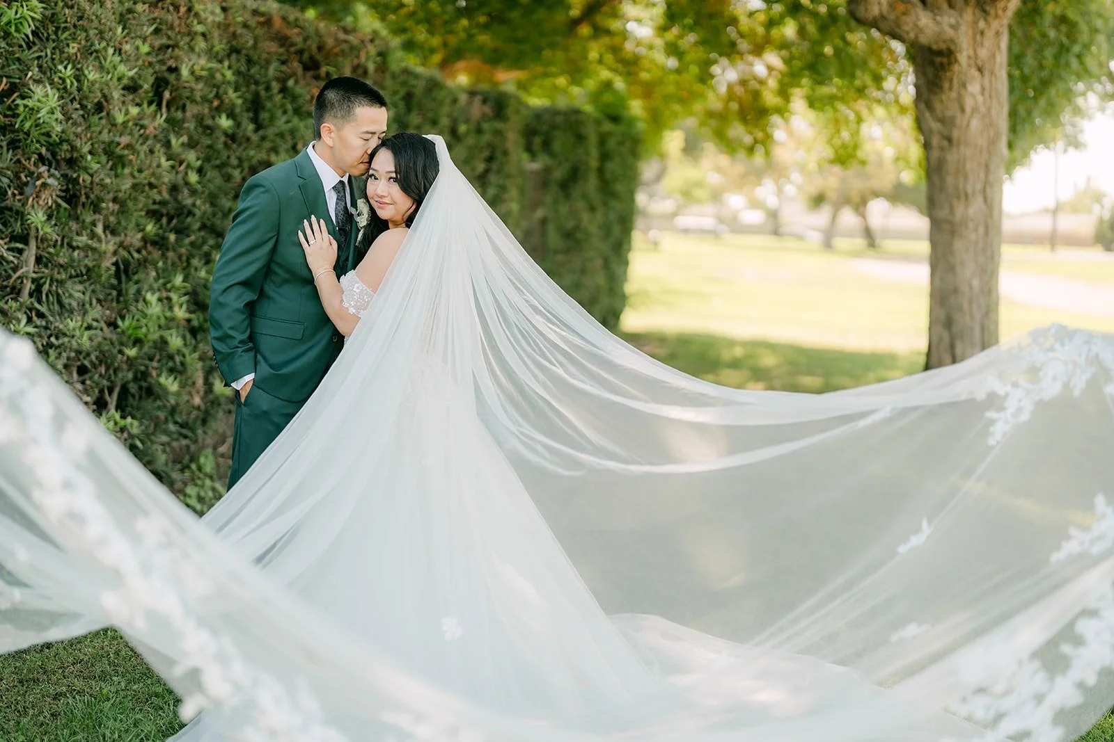 Jennifer's veil billows across the frame as she and Kevin embrace by the hedge