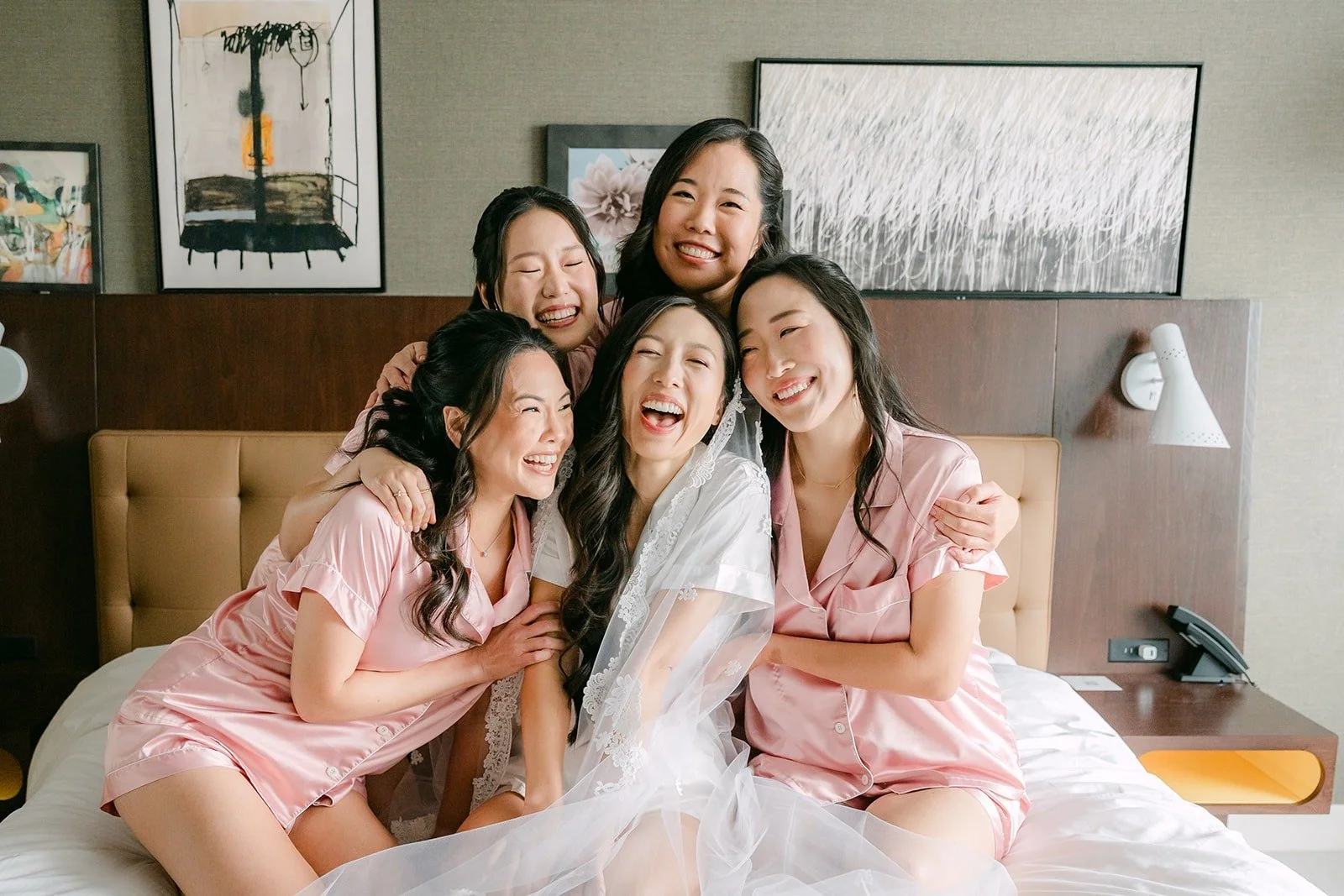 Kristine and her bridesmaids in blush satin pajamas piled on the hotel bed