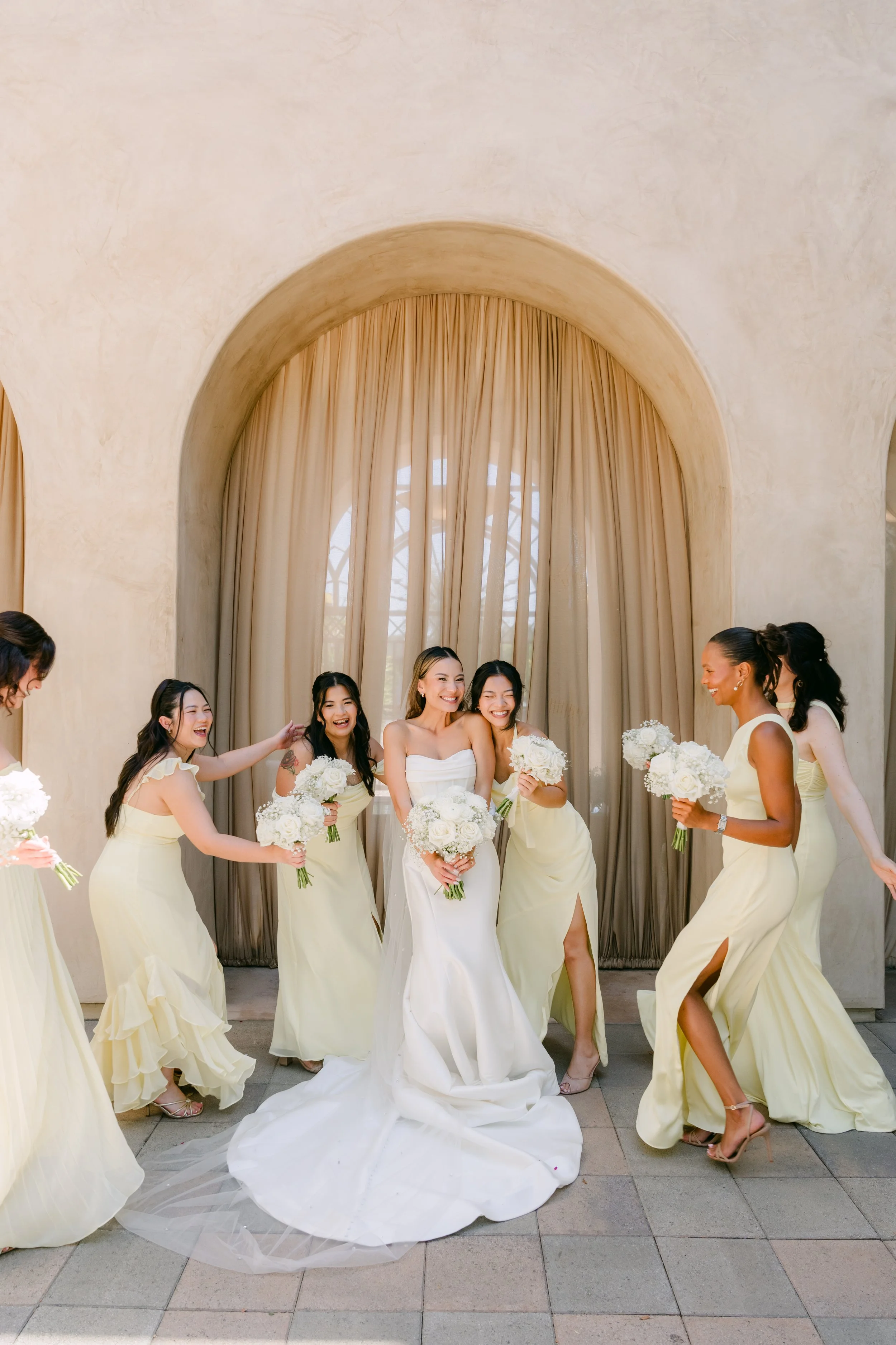 Kieu laughing with her bridesmaids in pale yellow gowns at Serra Plaza