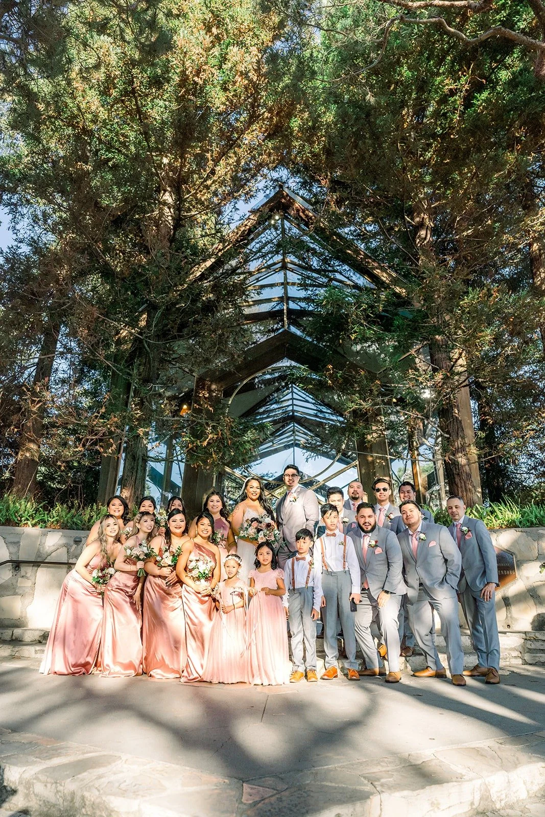 The full wedding party among the tall trees beside Wayfarers Chapel