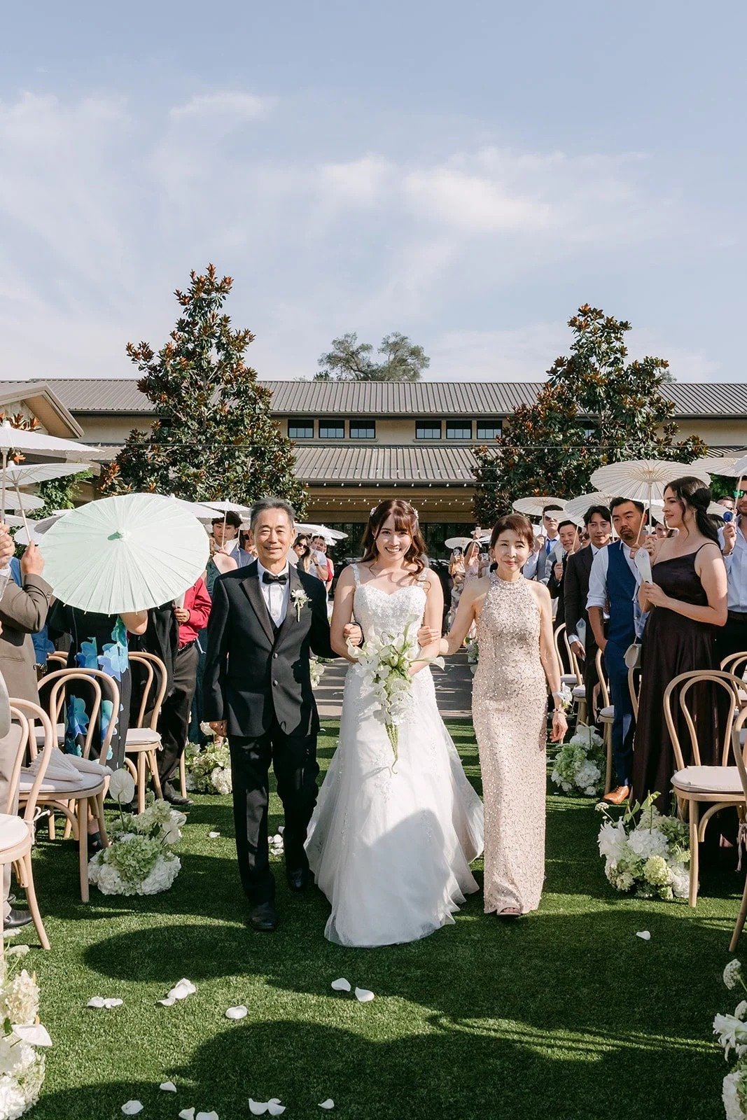 Marina walking down the aisle with her parents on the grass