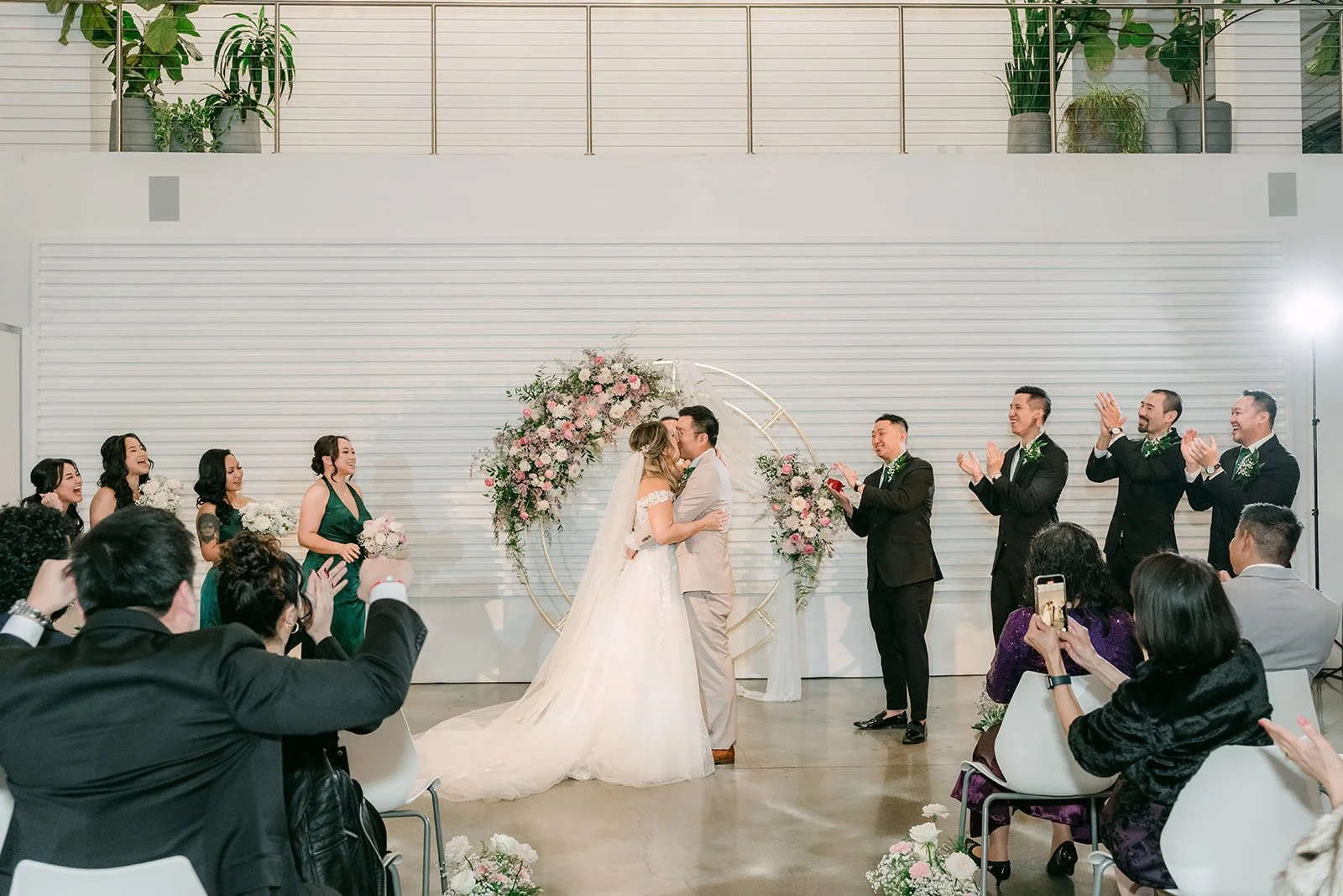 Guests cheering as Raine and Ricky kiss at the floral arch