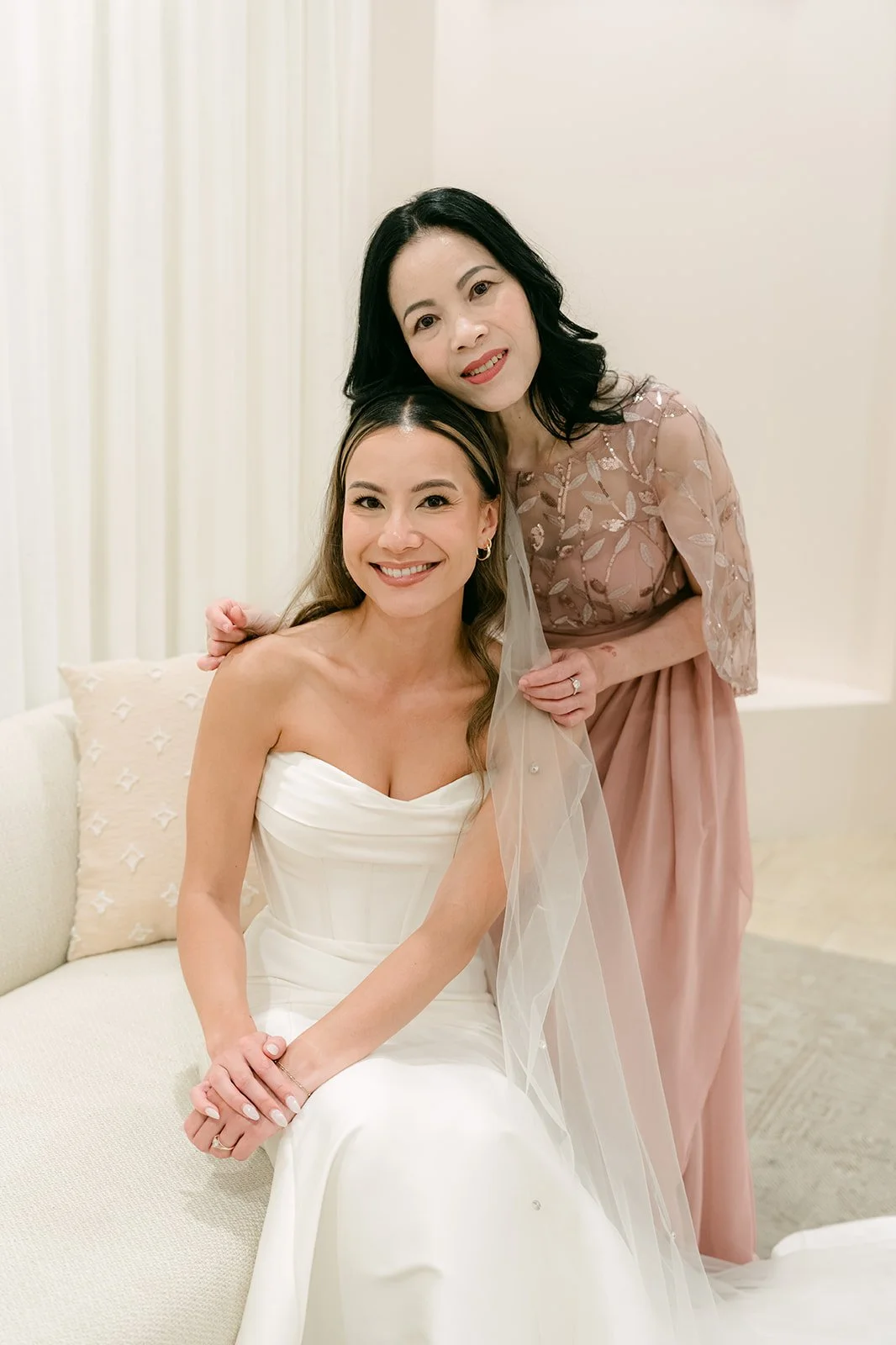 Bride smiling while her mother adjusts her veil in the bridal suite