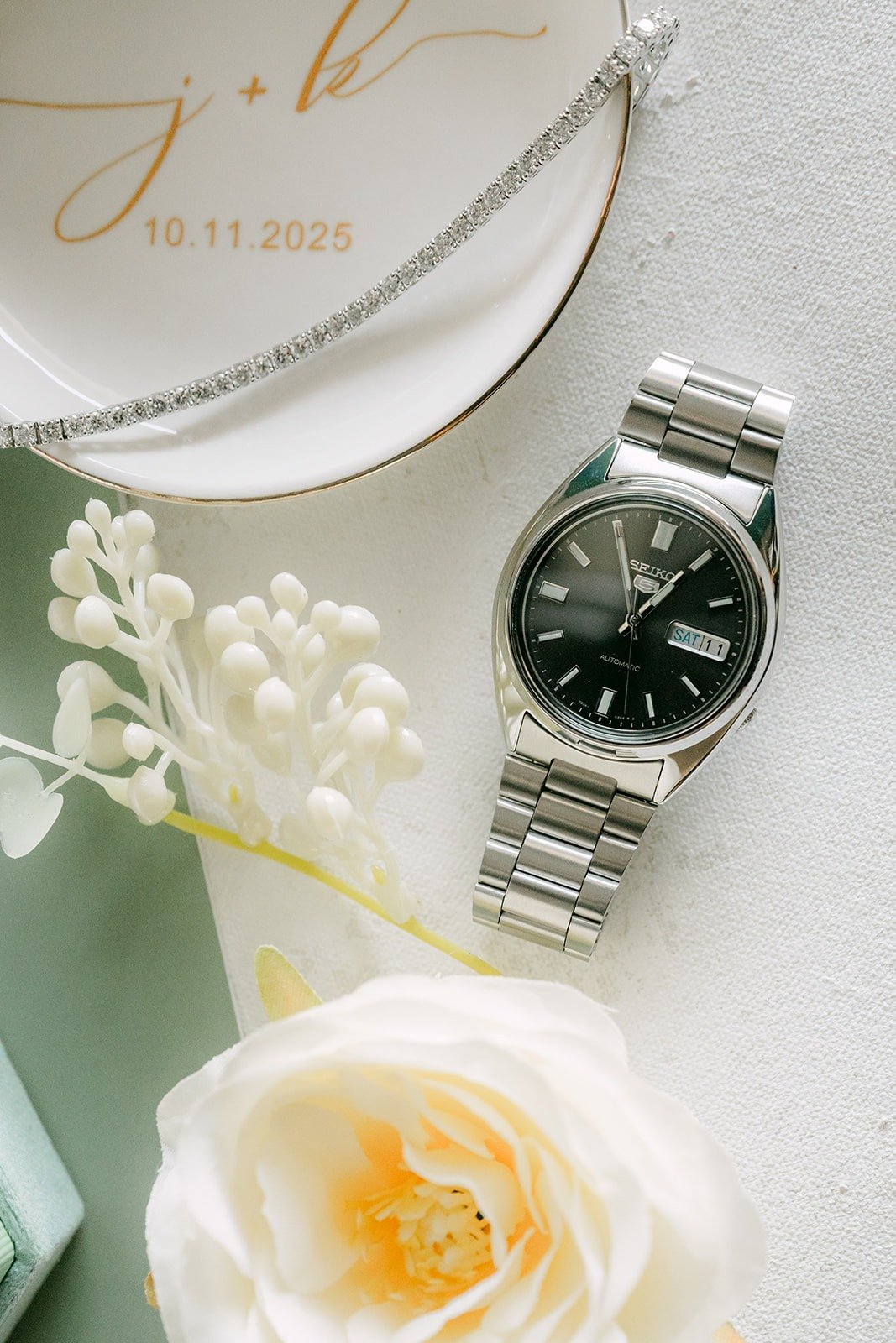 A silver watch styled with white flowers and a gold monogram card