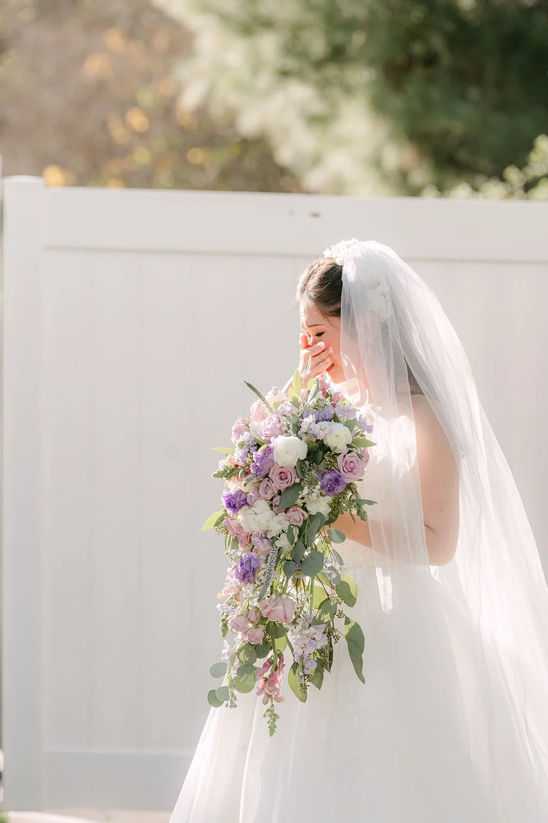 Kate holding her bouquet against a white fence.