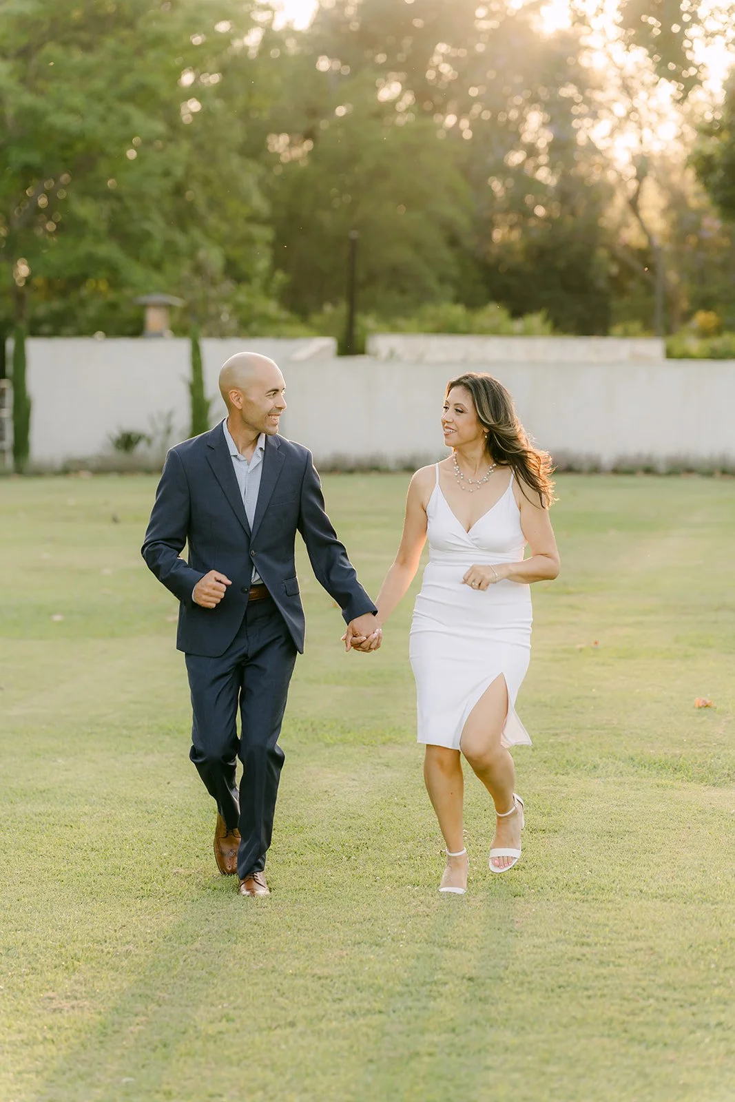 Francesca and Daniel walk across the lawn hand in hand at golden hour, photographed by One and Only Production.