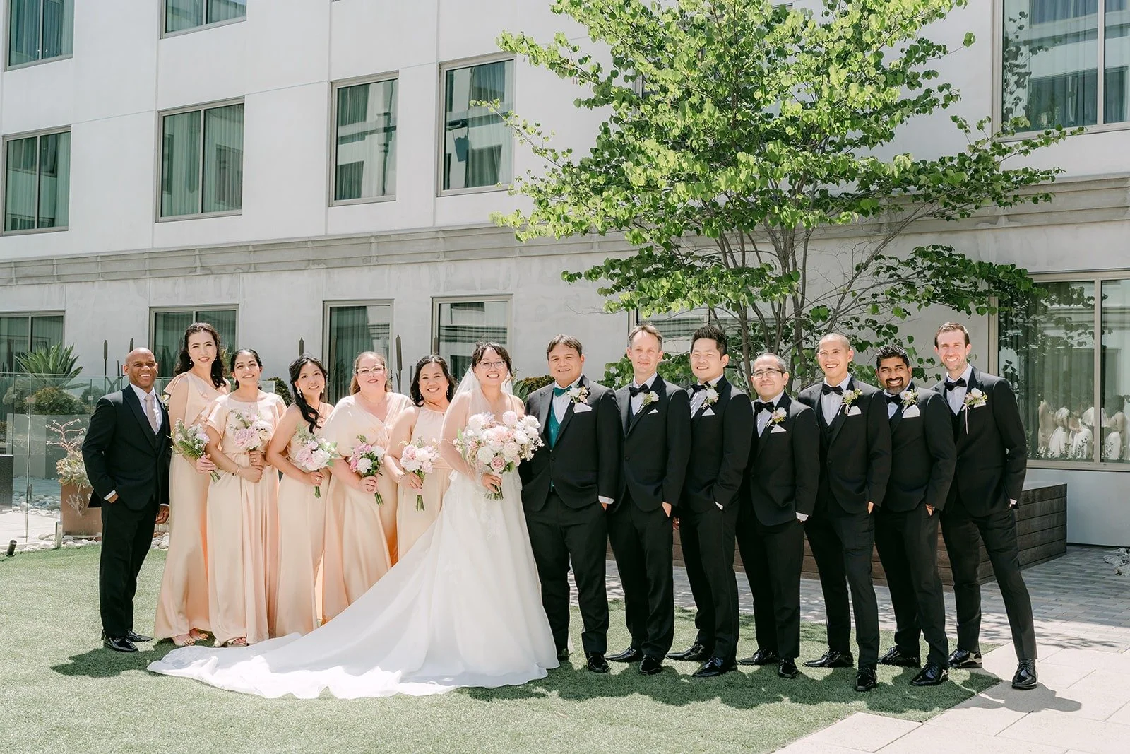 The full wedding party lined up on the courtyard lawn in champagne gowns and black tuxedos