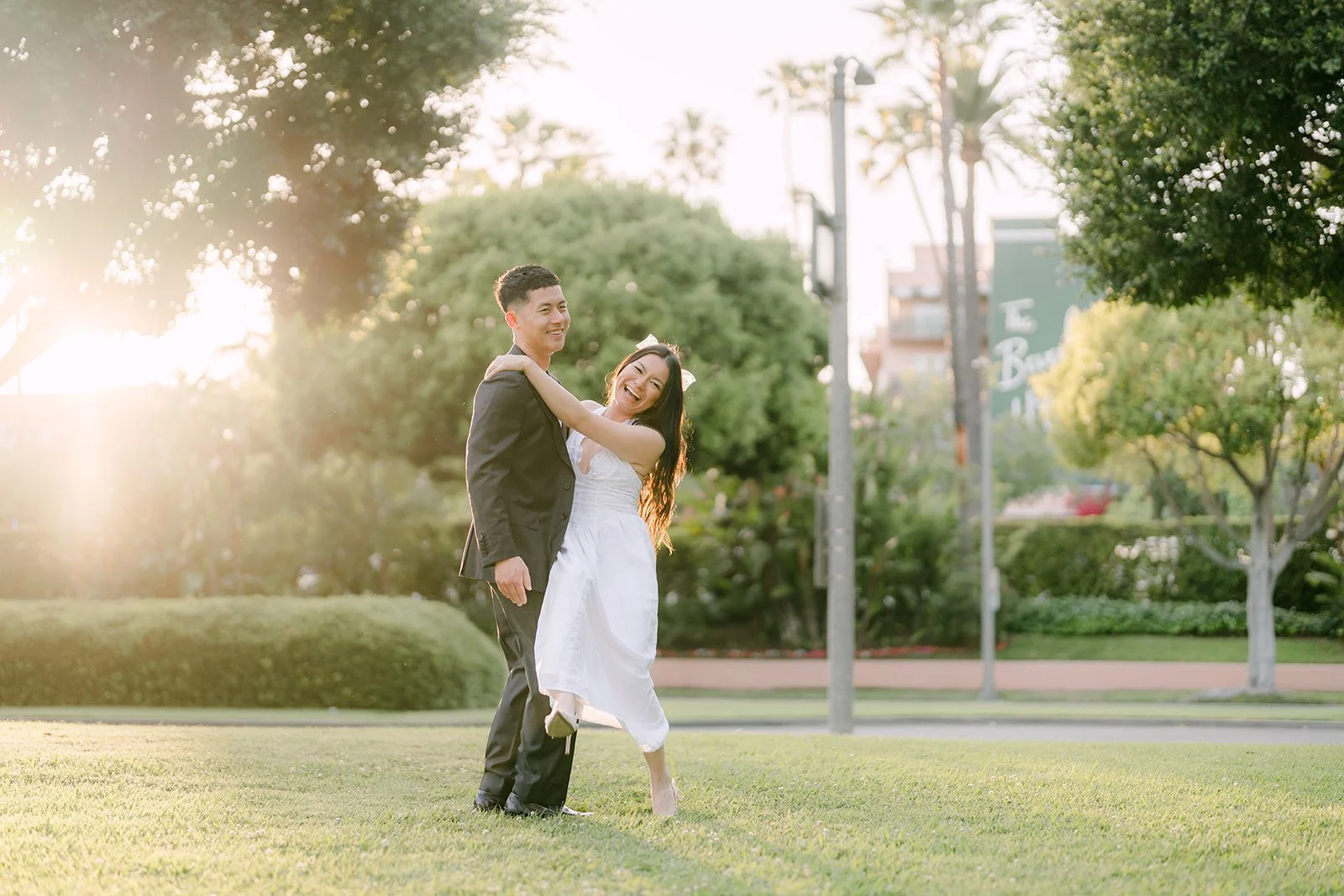 Jadee and Richard stand on the lawn as the sun glows through the trees.