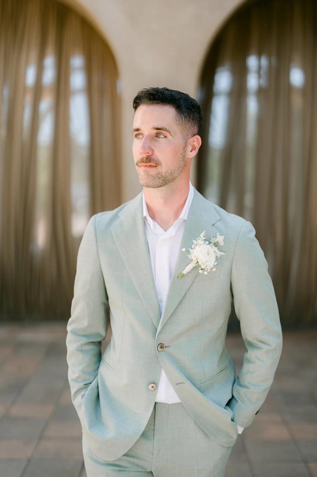 Groom in a sage suit with a white boutonniere looking off to the side
