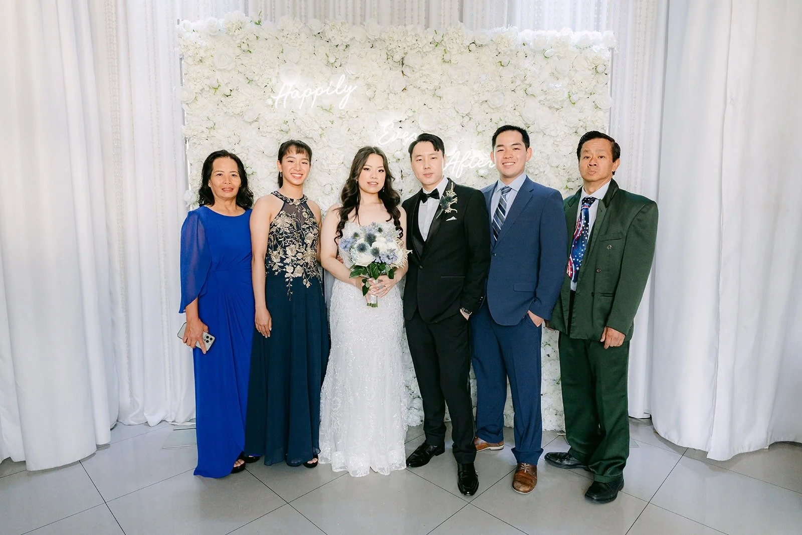 Emily and James with guests in front of the white flower wall