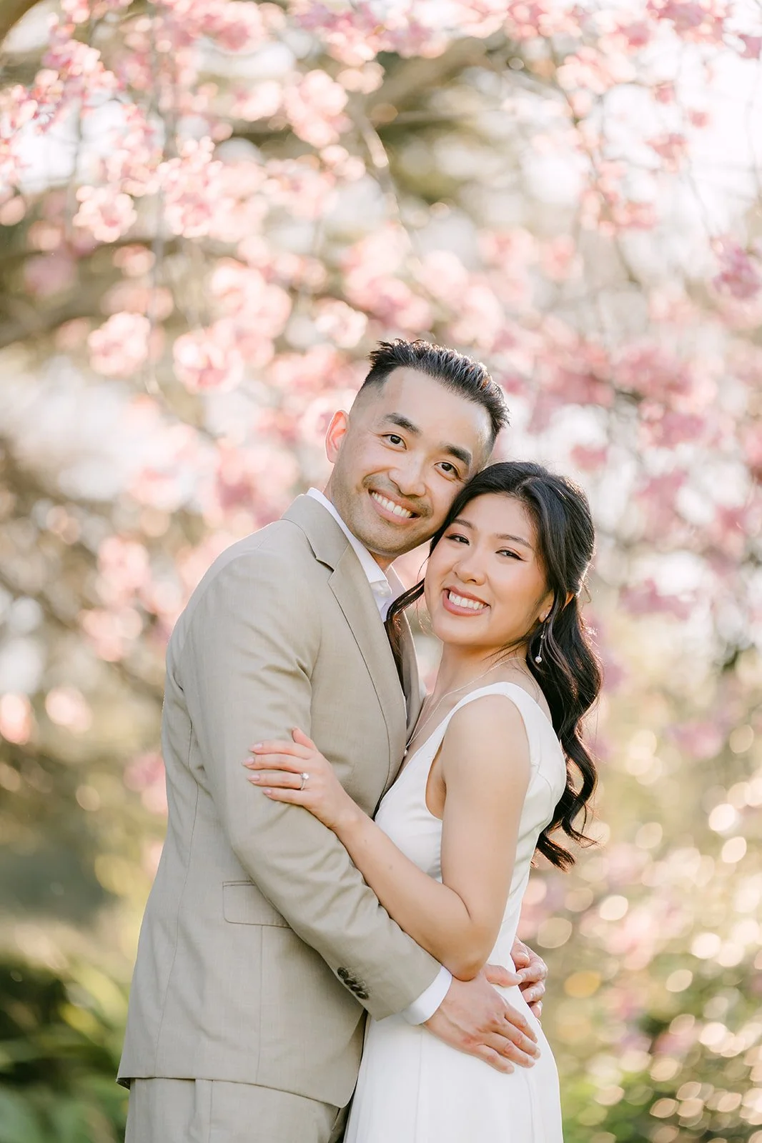 Vincent holds Kim as they laugh beneath the pink blossoms.