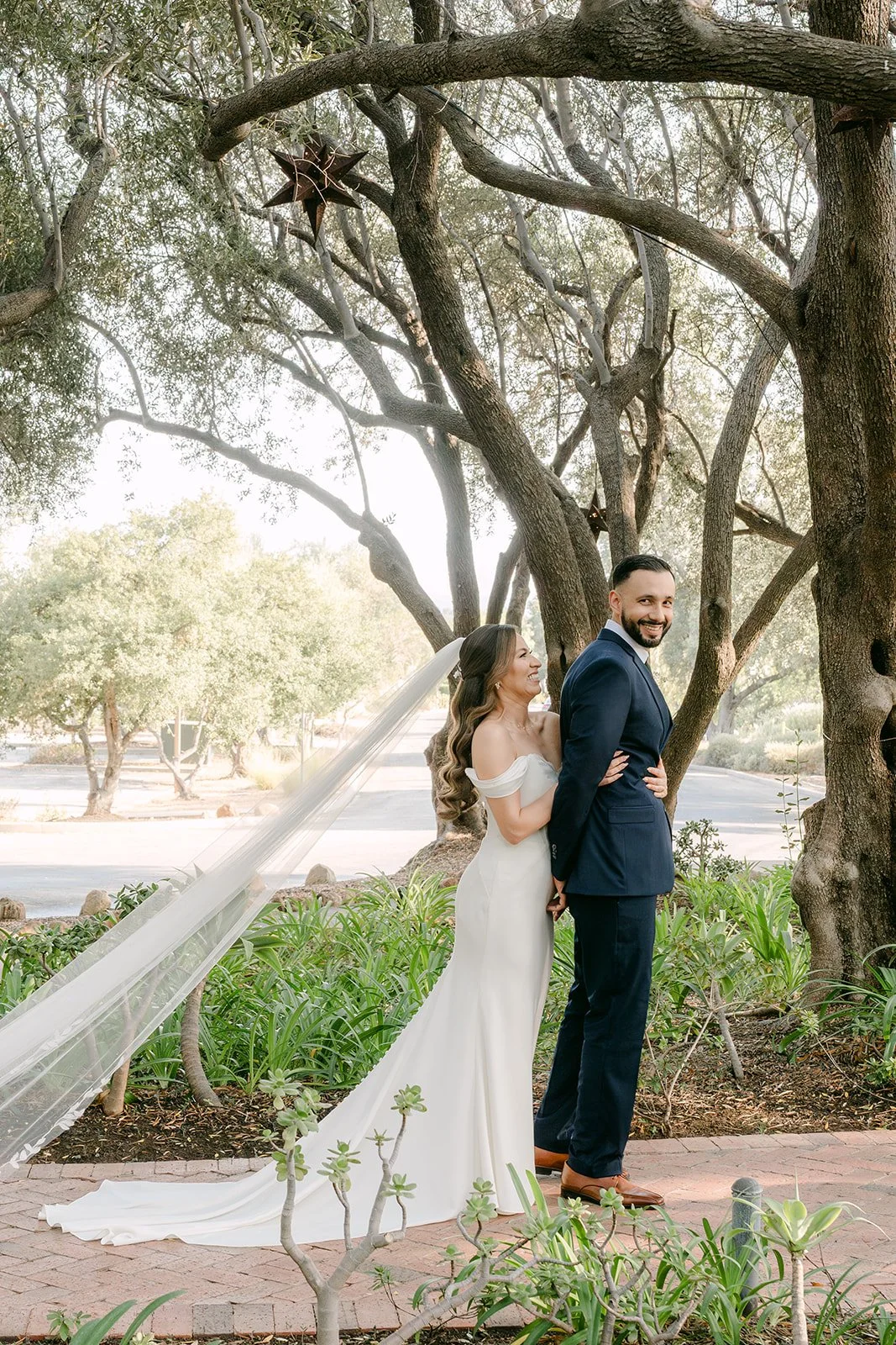 Mariana and Danny facing each other under the olive trees, her veil trailing behind
