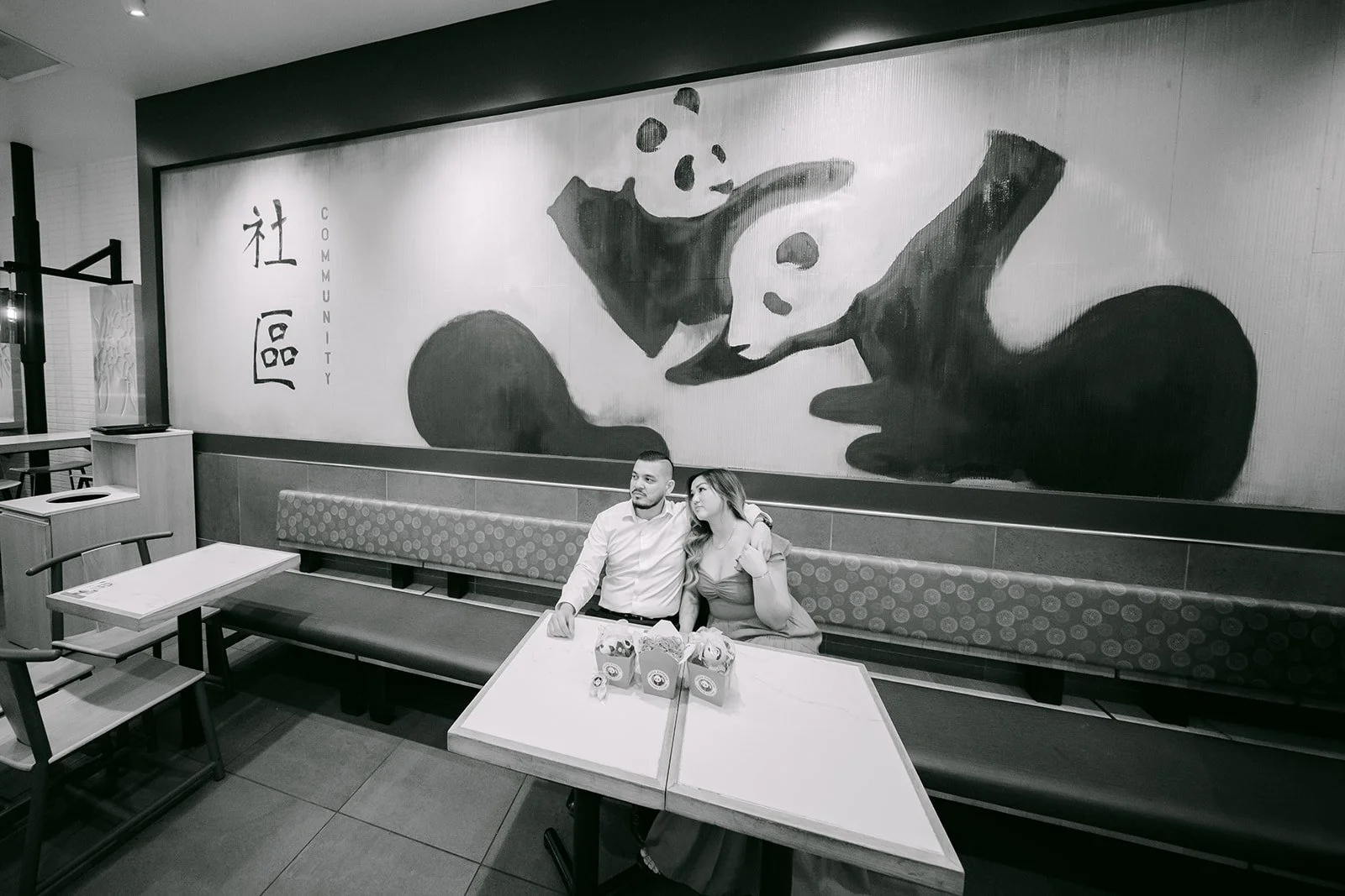 Black and white photo of Linh and Ankush at a table beneath a panda mural.
