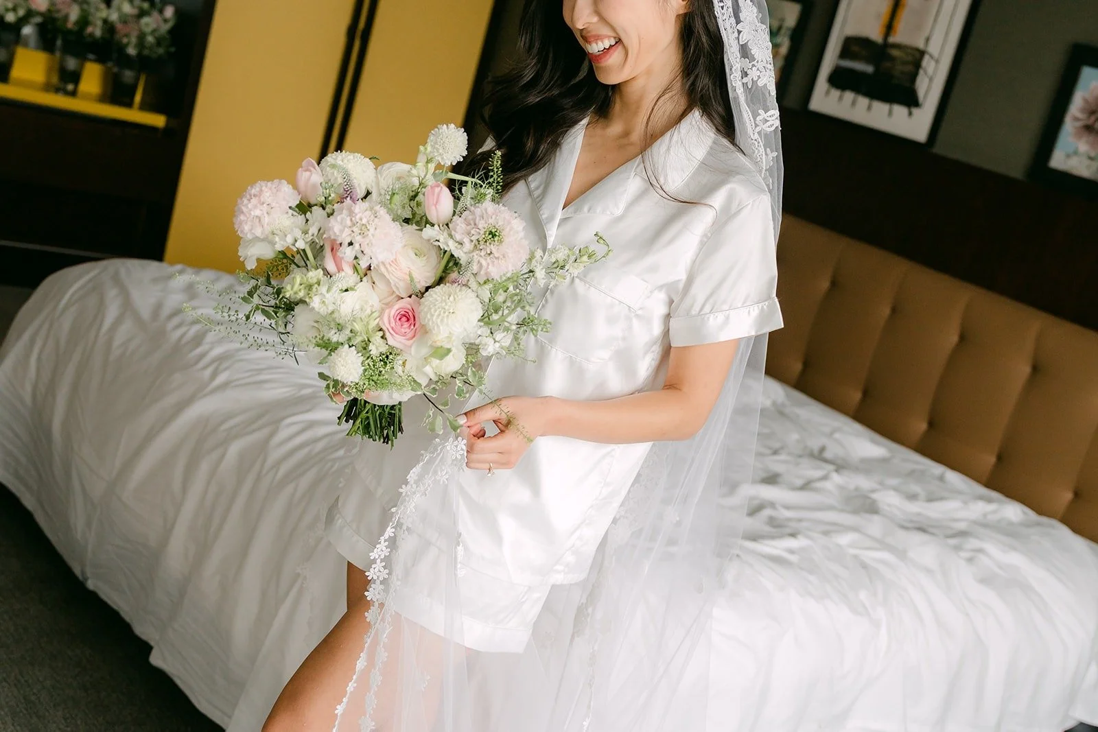 Kristine sitting on the bed in her robe with her blush and ivory bouquet