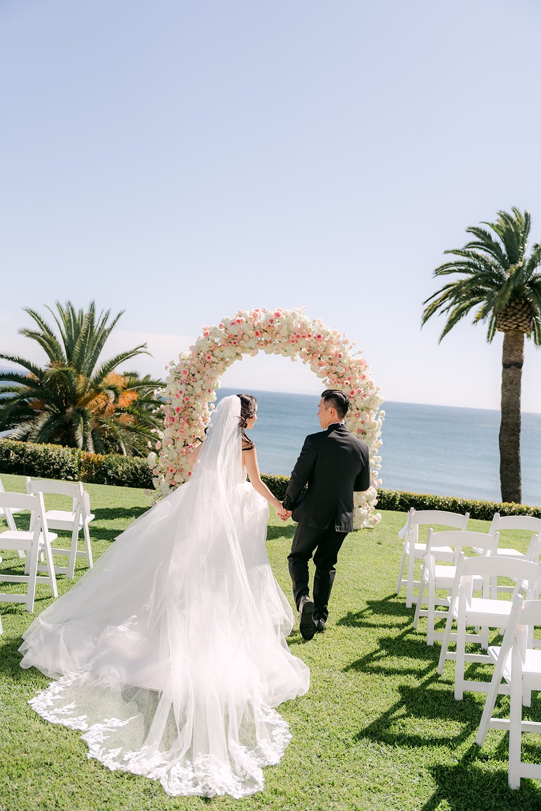 Couple walking down the aisle toward the arch and the ocean