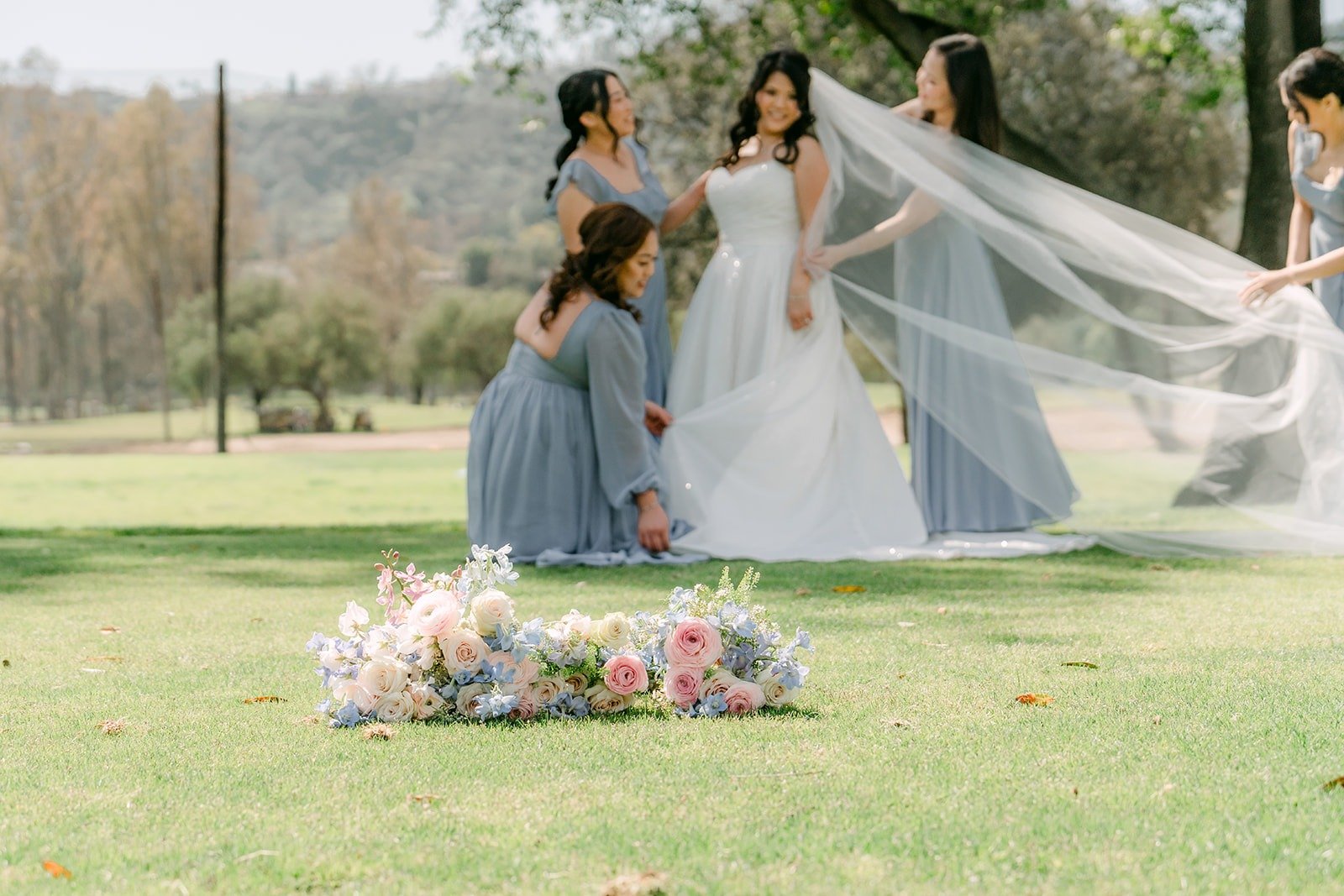 Florence and her bridesmaids spreading out her long veil on the lawn