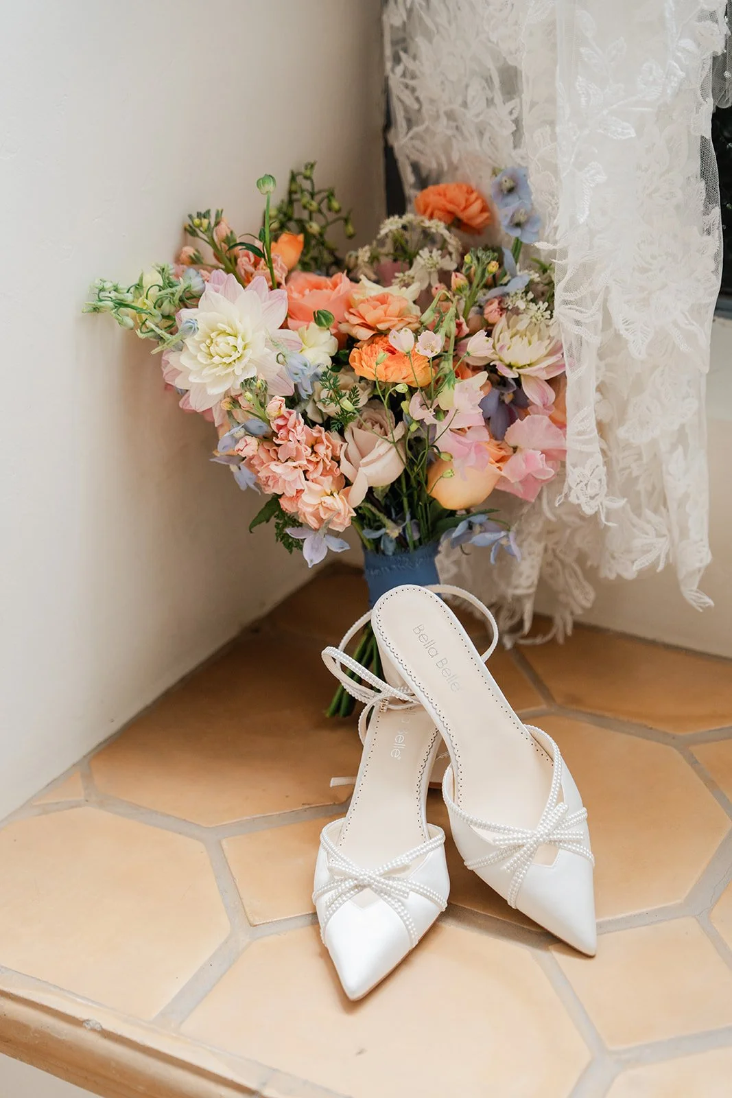 Peach and blue bouquet resting beside the bride's heels in a sunlit corner